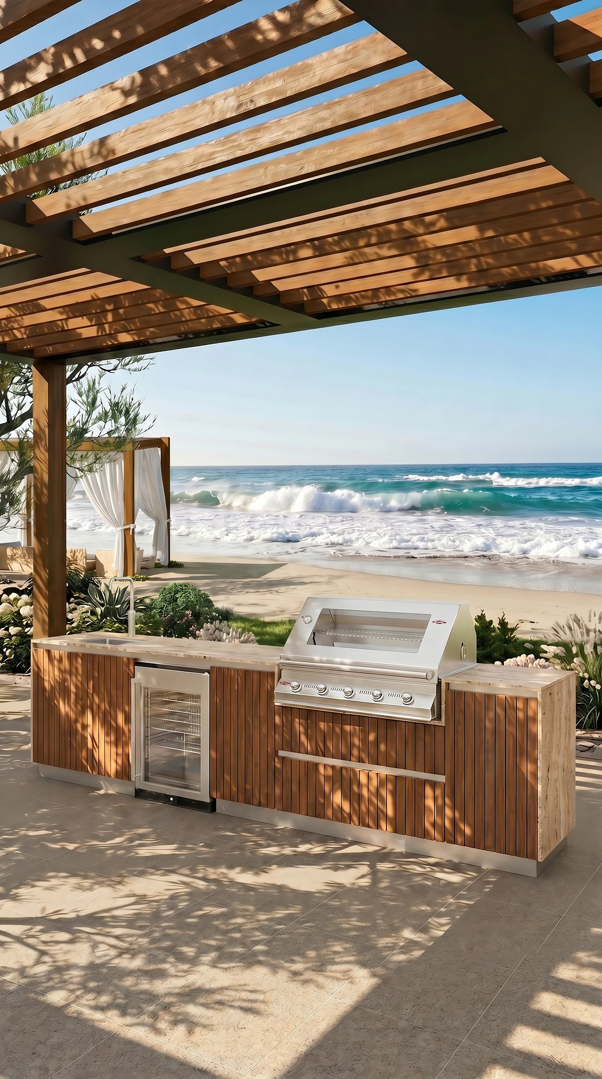 Al Fresco Kitchenette with teak cabinetry, travertine countertop, stainless steel grill, sink and mini fridge beneath a beachside pergola.