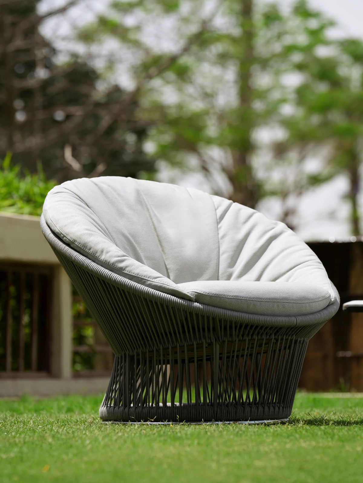 Angled view of the Sun outdoor armchair with a dark grey handwoven rope frame and light cushioned interior on a garden lawn.