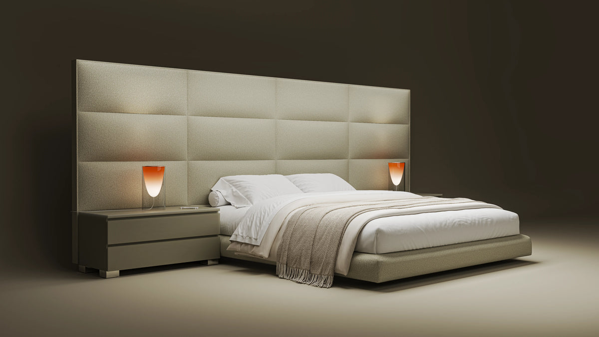 Angled view of the beige Platinum bed with a curved upholstered platform, bombé cladding, and matching nightstands.
