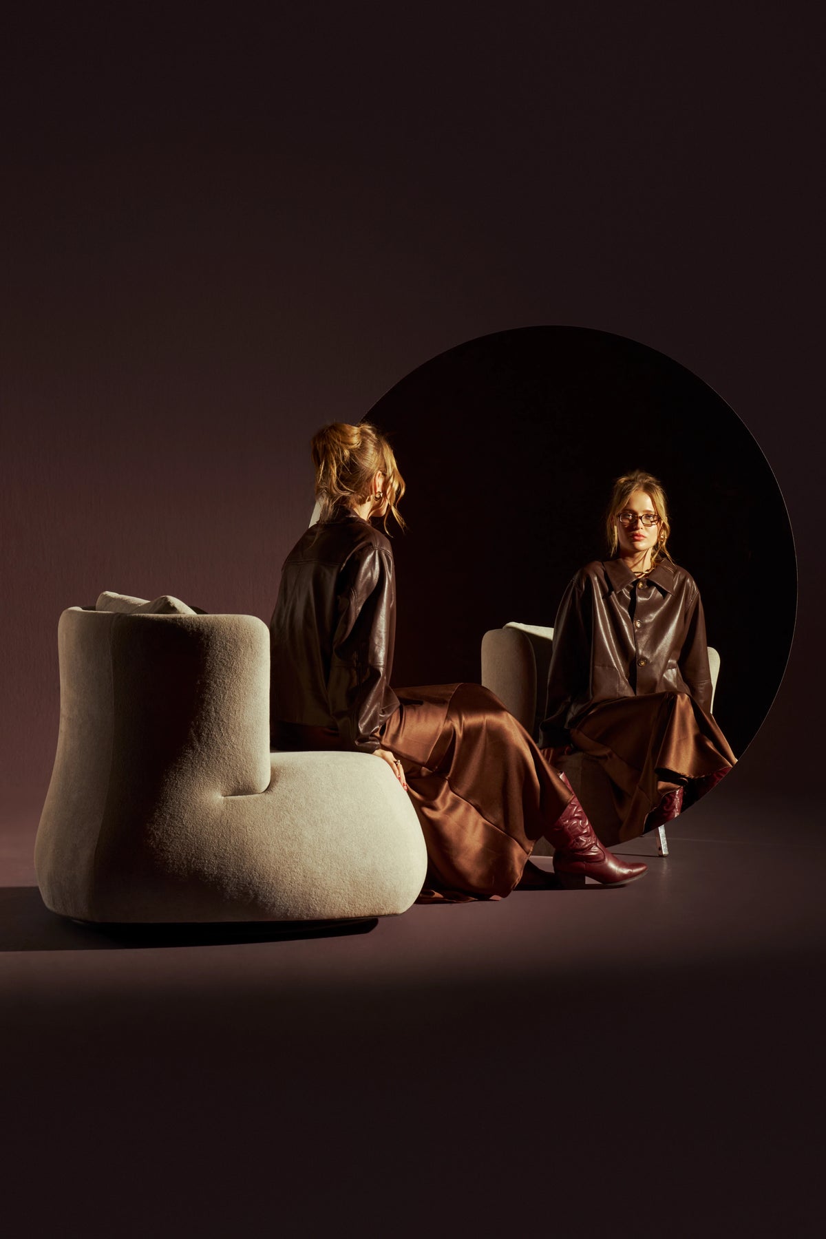 Woman seated in the cream Belly armchair, with its rounded back and wraparound sides reflected in a circular mirror.