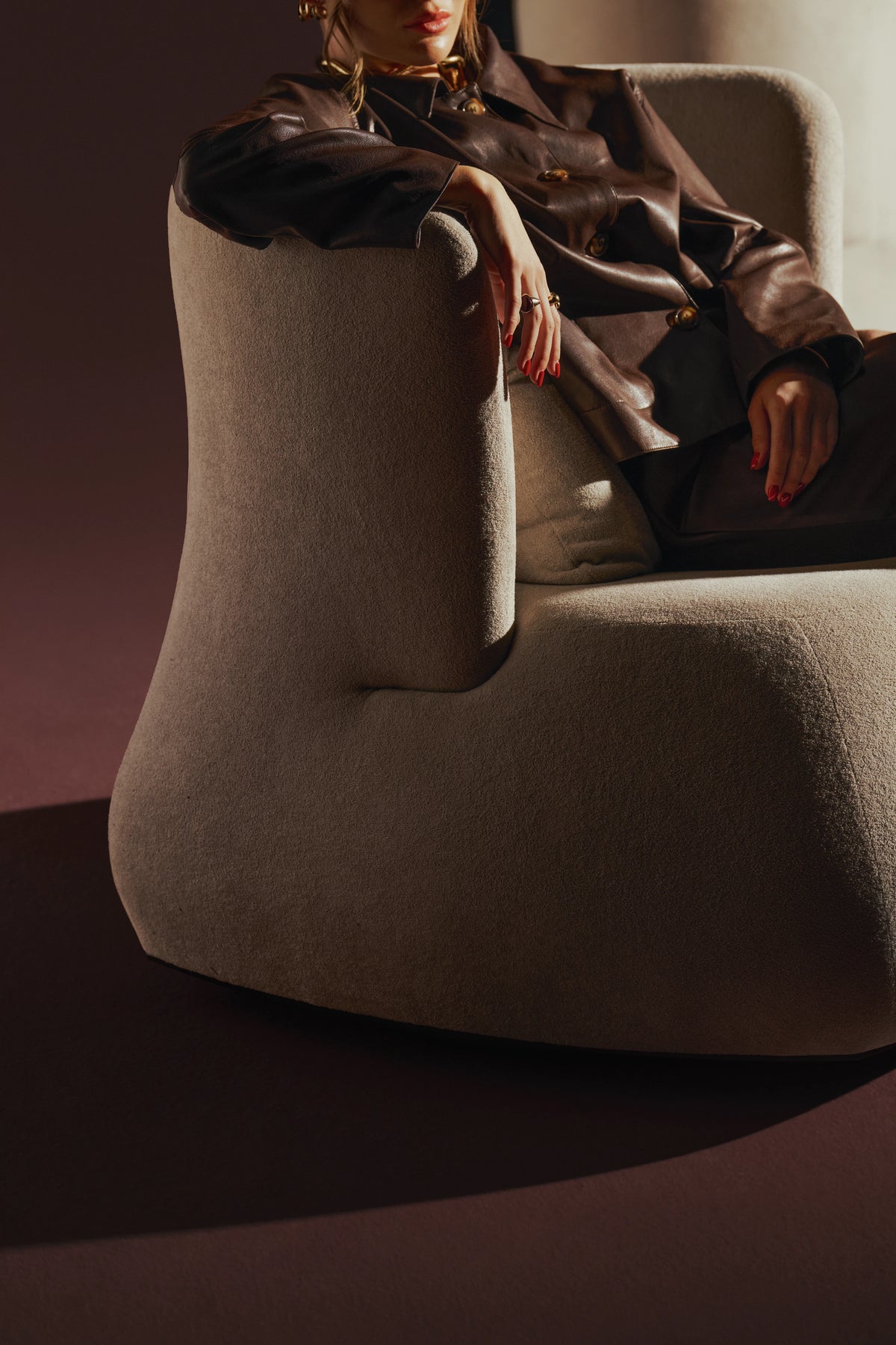 Close-up of the cream Belly armchair with a seated woman, highlighting its curved side and rounded upholstered base.