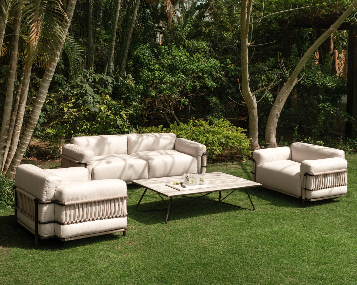 Bloom outdoor sofa set with cream upholstered cushions, stainless steel frame, electrostatic-coated legs, and hand-woven rope detailing along the sides, styled in a garden setting with matching armchairs and Geo table.