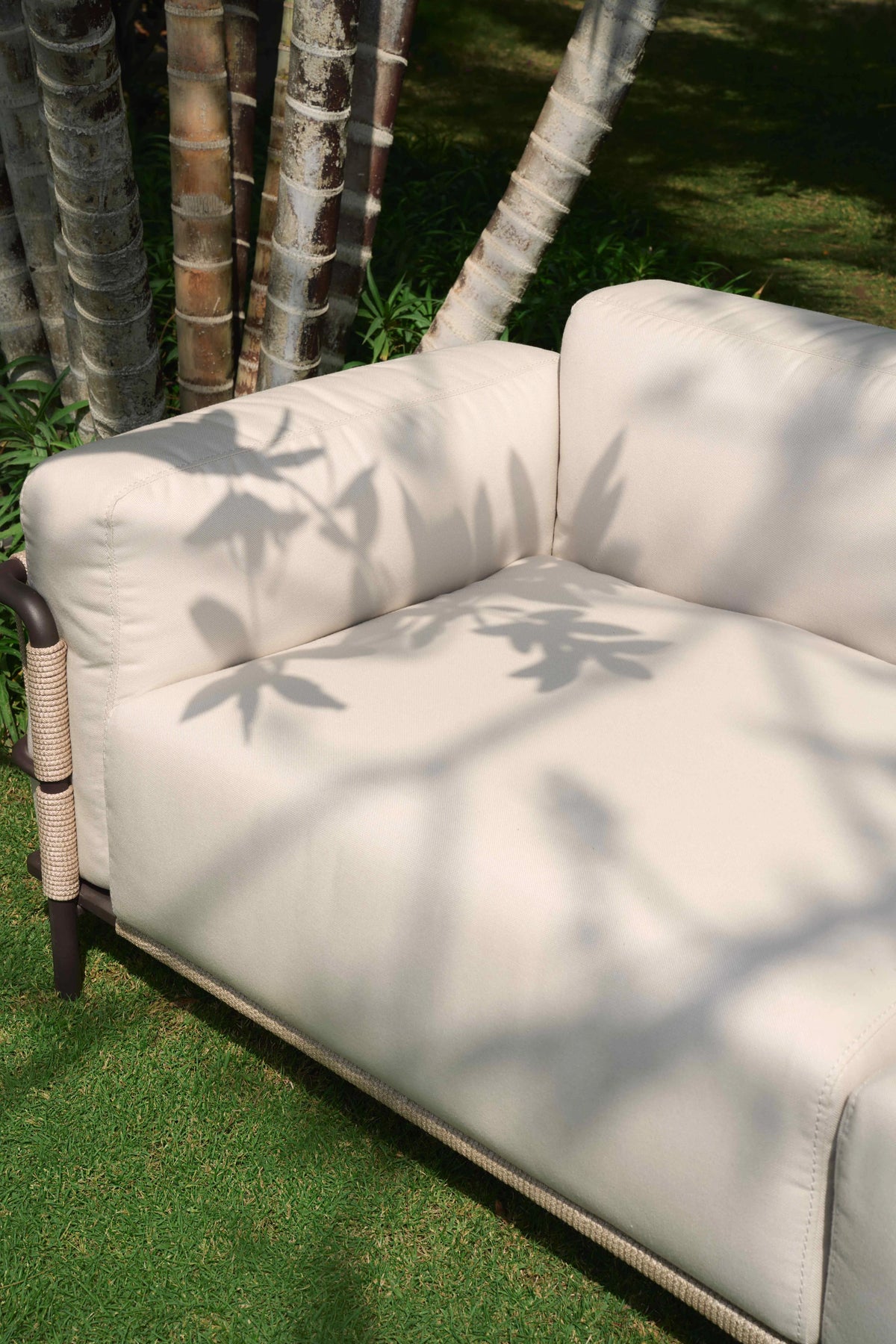 Close-up of the cream Bloom outdoor sofa’s seat, backrest, and arm cushions beside its rope-wrapped stainless steel frame.