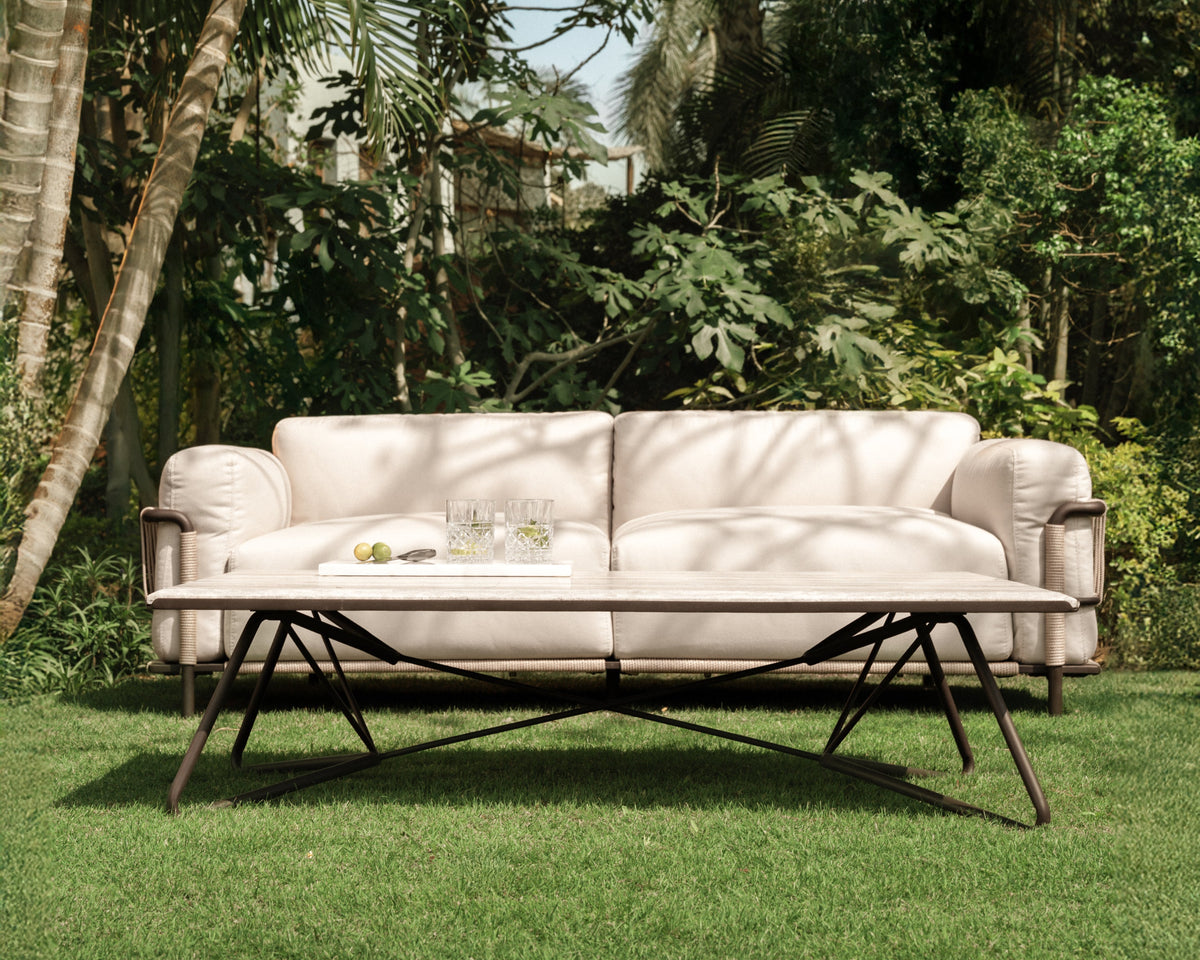 Front view of Bloom sofa in cream upholstery, featuring stainless steel frame with electrostatic-coated legs and hand-woven rope detailing across the arms, styled outdoors on a lawn with Geo coffee table.