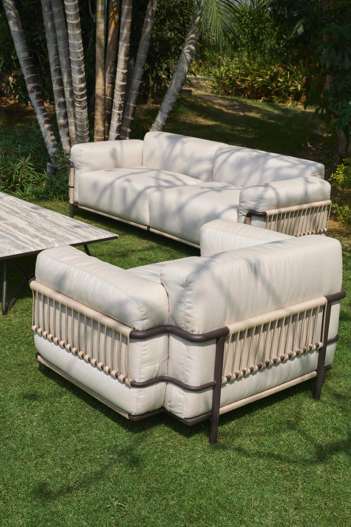 Rear view of the cream Bloom outdoor sofa and armchair, highlighting the handwoven beige rope and dark stainless steel frames.