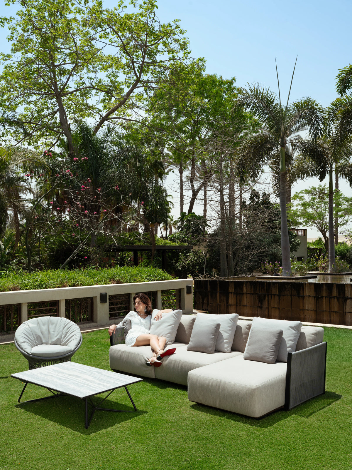 Beige Caribbean sectional sofa with grey rope sides and layered cushions, paired with a Sun armchair and Geo coffee table on a garden lawn.