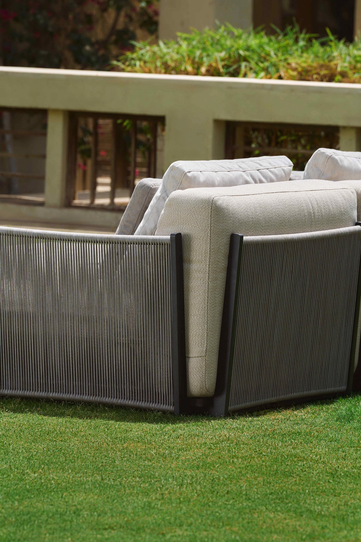 Close rear view of the Caribbean outdoor sofa showing its grey handwoven rope panels, dark stainless steel frame and beige cushions.