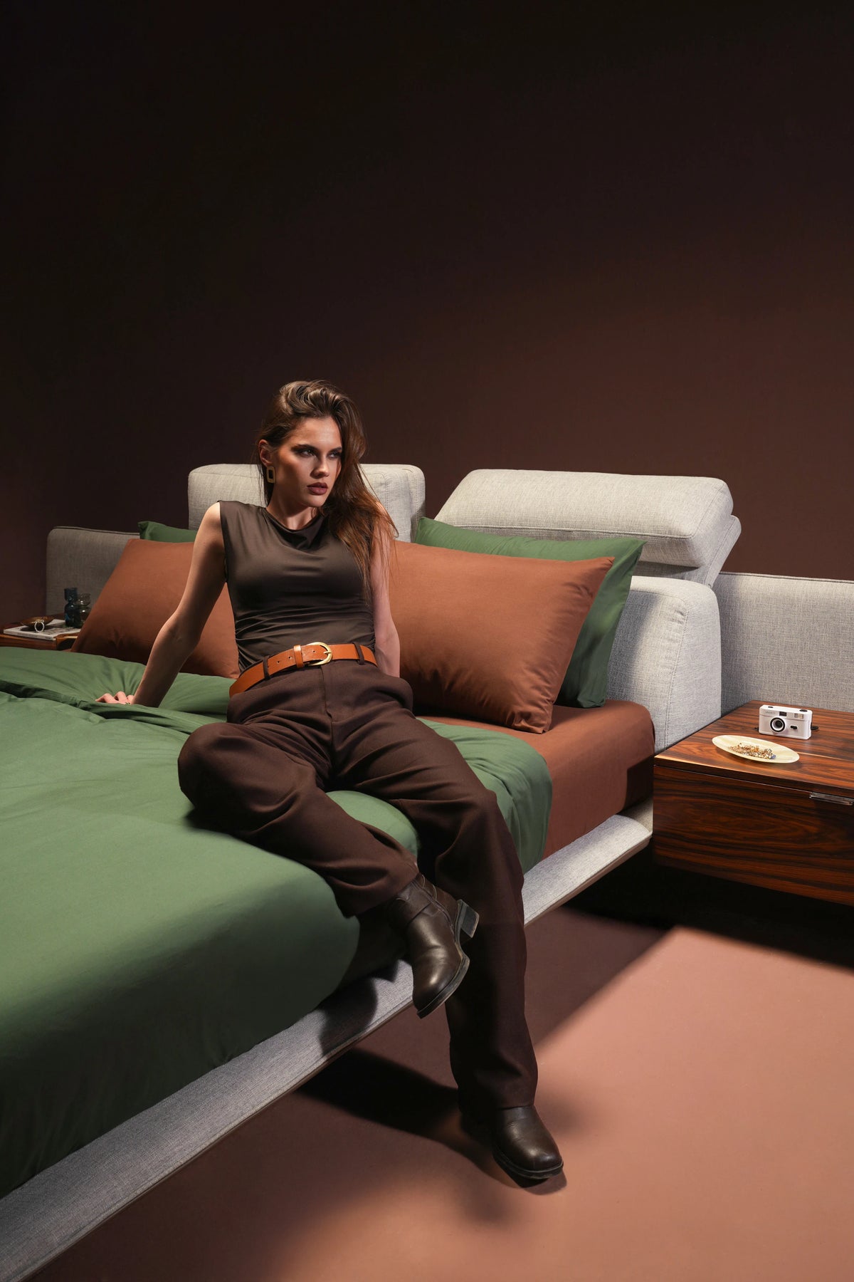 Model seated on Chill Bed in grey fabric, highlighting soft upholstered cladding and platform mattress design.
