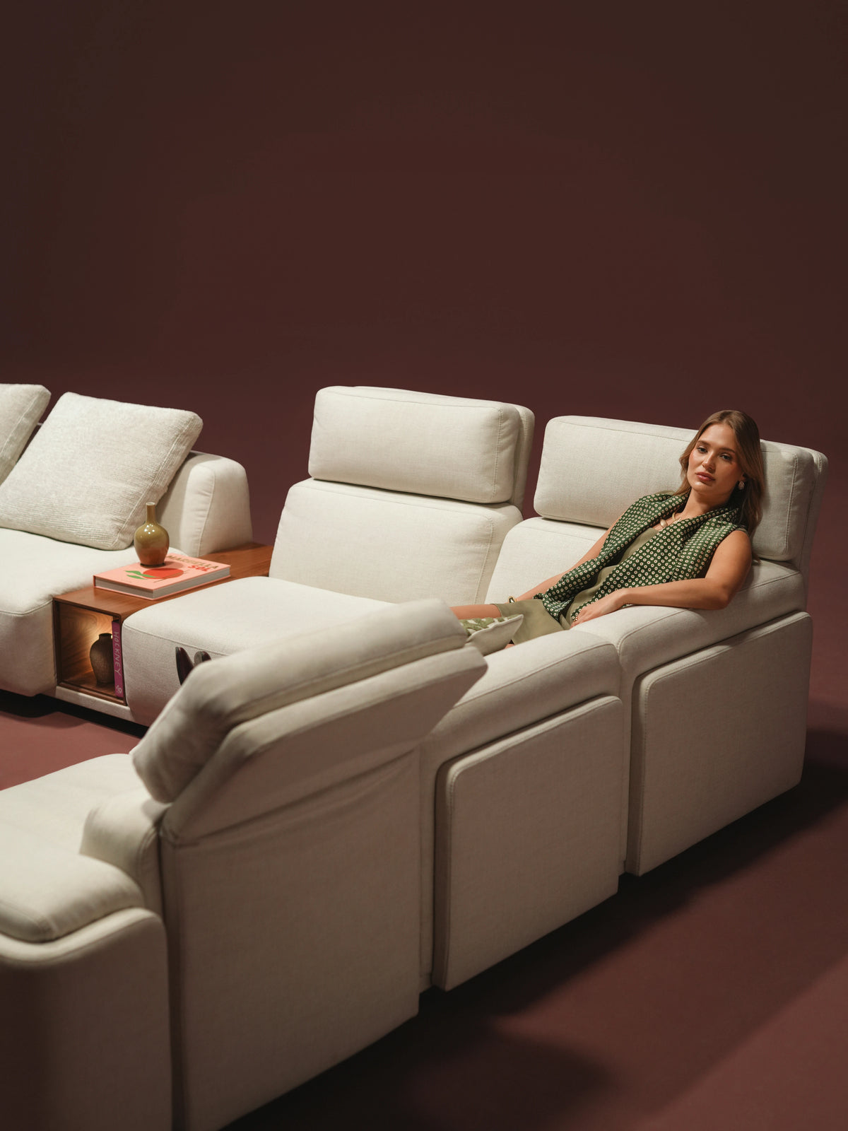 Woman seated on the ivory Chill sofa with raised adjustable headrests and an integrated wooden table.