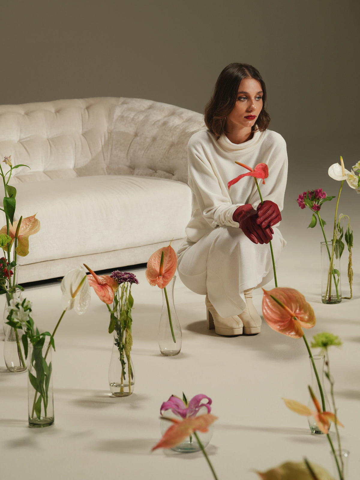 Woman seated in front of the beige Cloud sofa, styled with colorful flowers that frame its curved form and capitonné tufting.