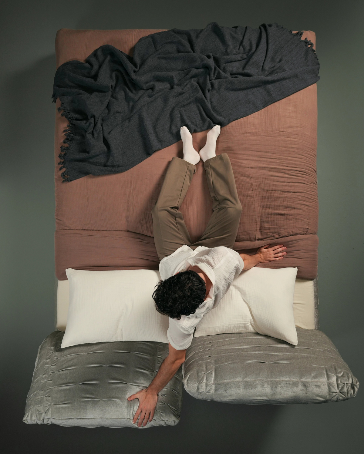 Overhead view of a man lying on the Crusty bed with one side of the pleated backrest extended outward for relaxed support.