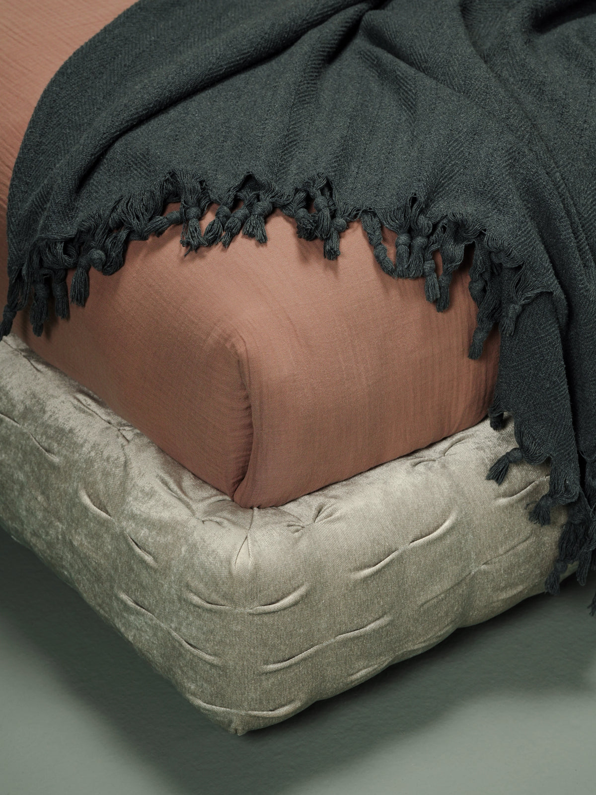 Close view of the Crusty bed’s rounded upholstered platform with hand-stitched pleating, brown bedding and a dark grey throw.