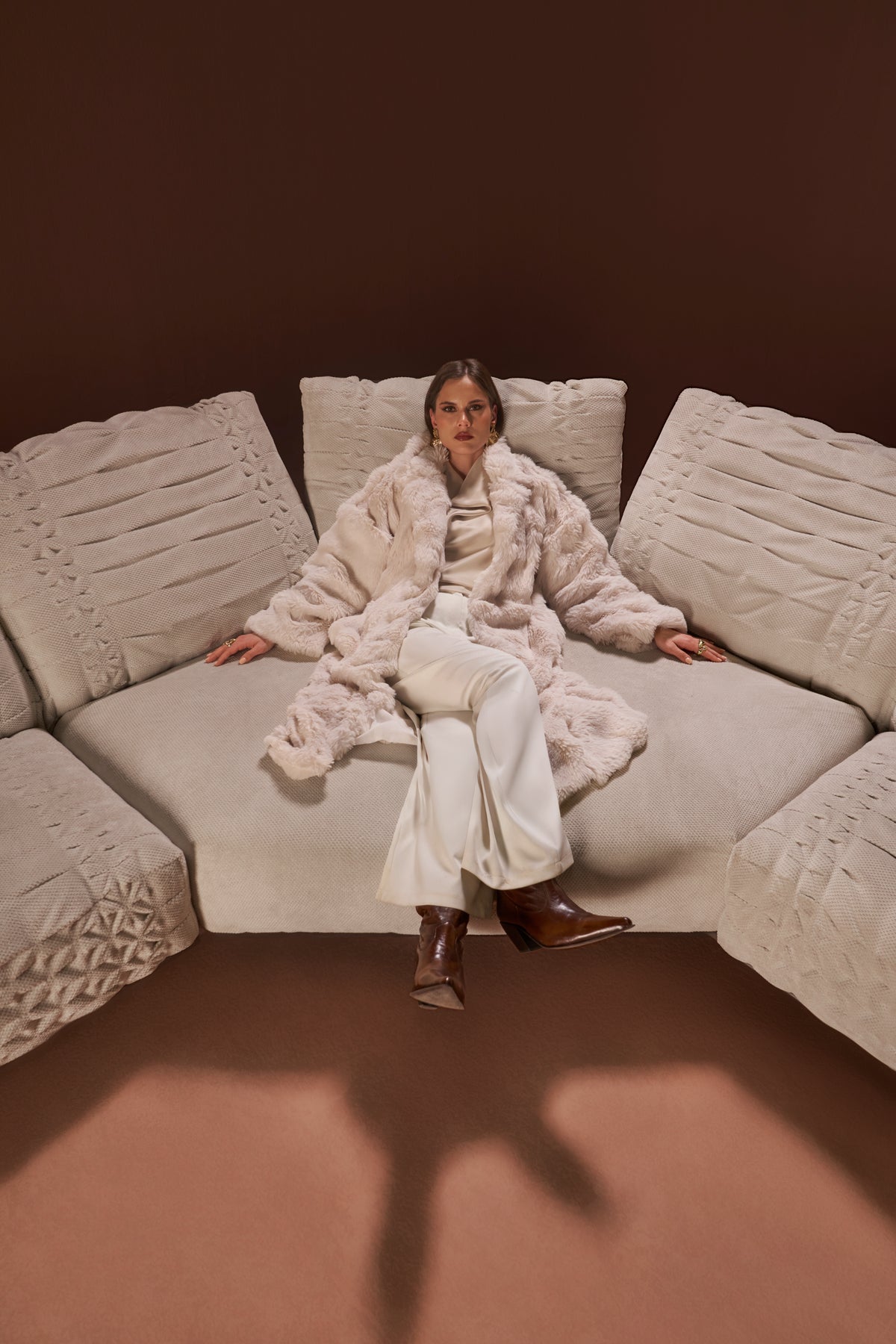 Model seated in the center of the Crusty sectional sofa in textured fabric, showing deep seats and stitched detail.