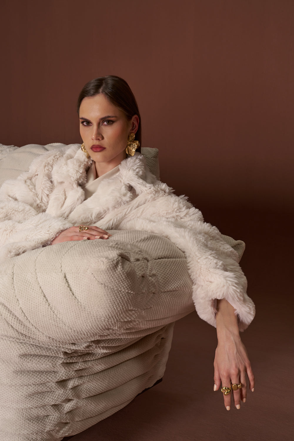 Model leaning on the Crusty sofa arm in textured fabric, highlighting adjustable armrest and bold pleated stitching.