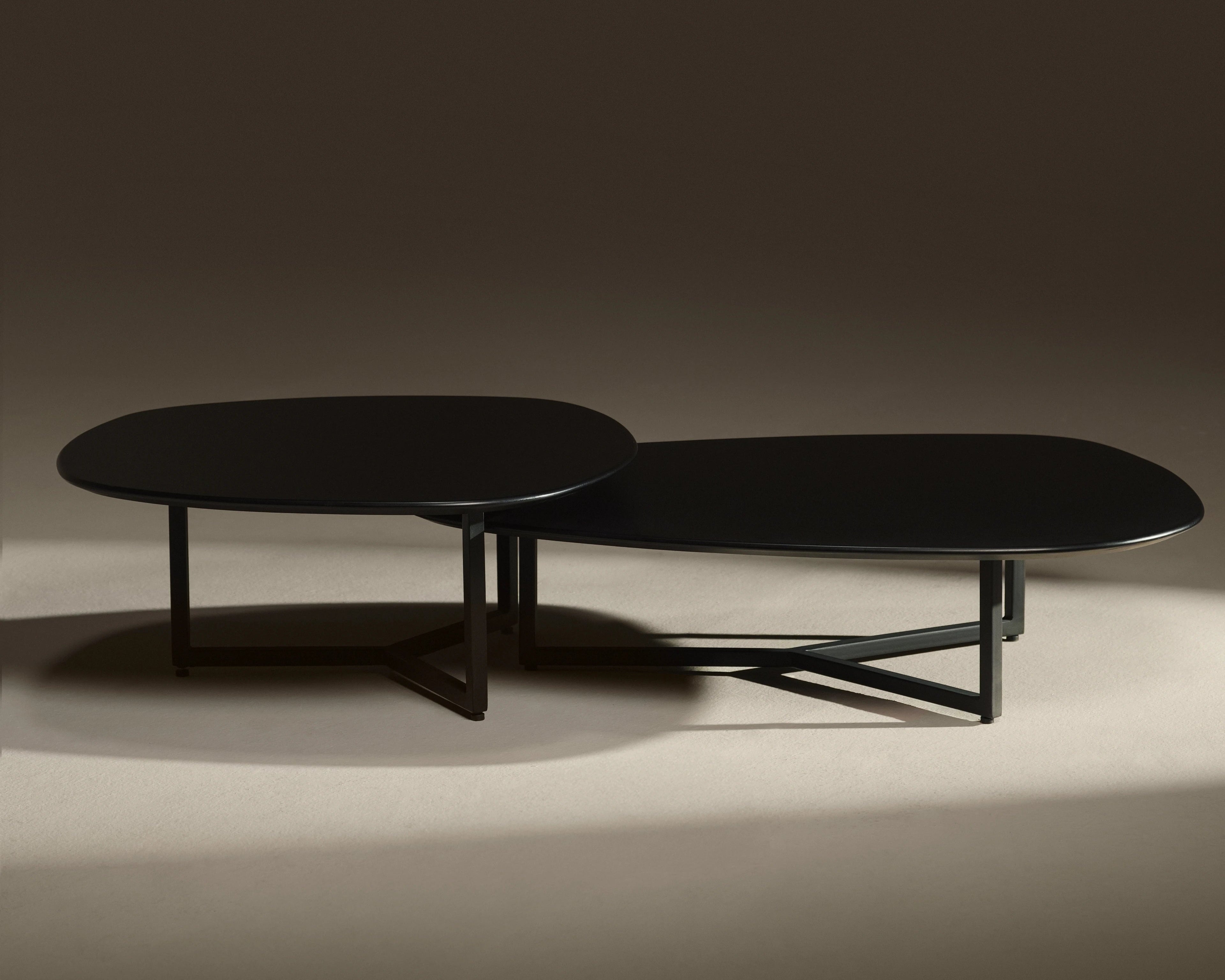 A modern black coffee table with an organic, flowing silhouette and angular metal legs, photographed against a dark beige studio background.