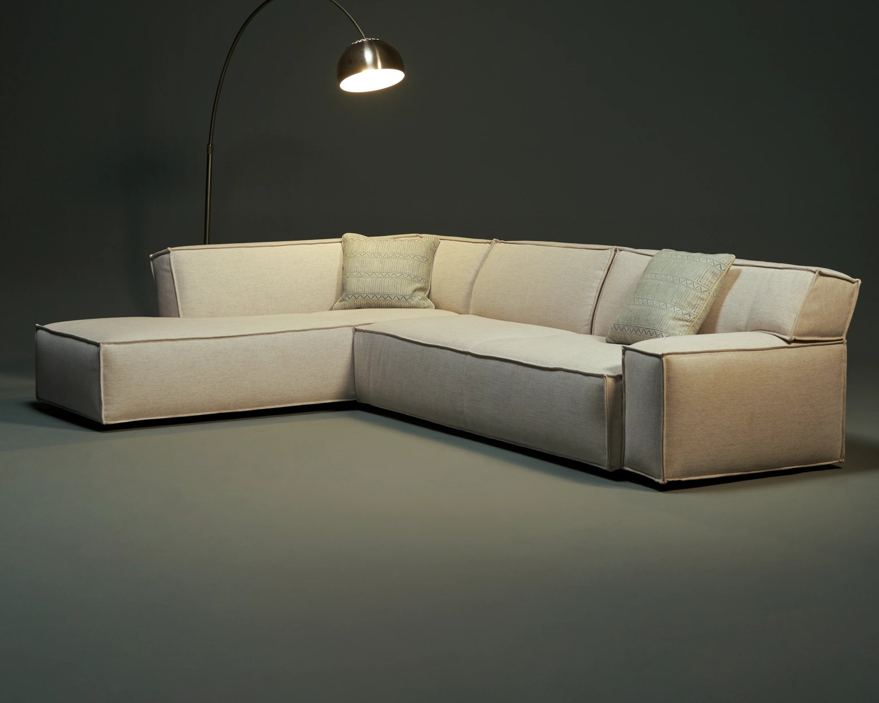 Front view of the beige Da-Fluff Alto sectional sofa with a chaise lounge, slanted backrest, wide arms, and French seam detailing.