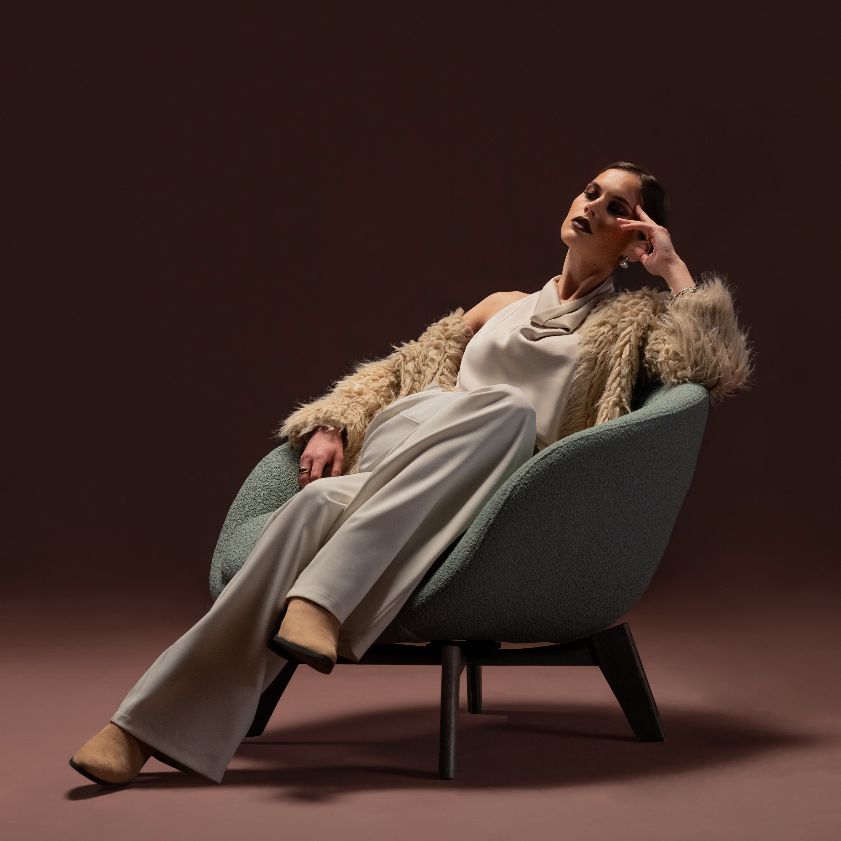 Model reclining in the Darby armchair upholstered in textured green fabric with rounded form and solid oak leg base.