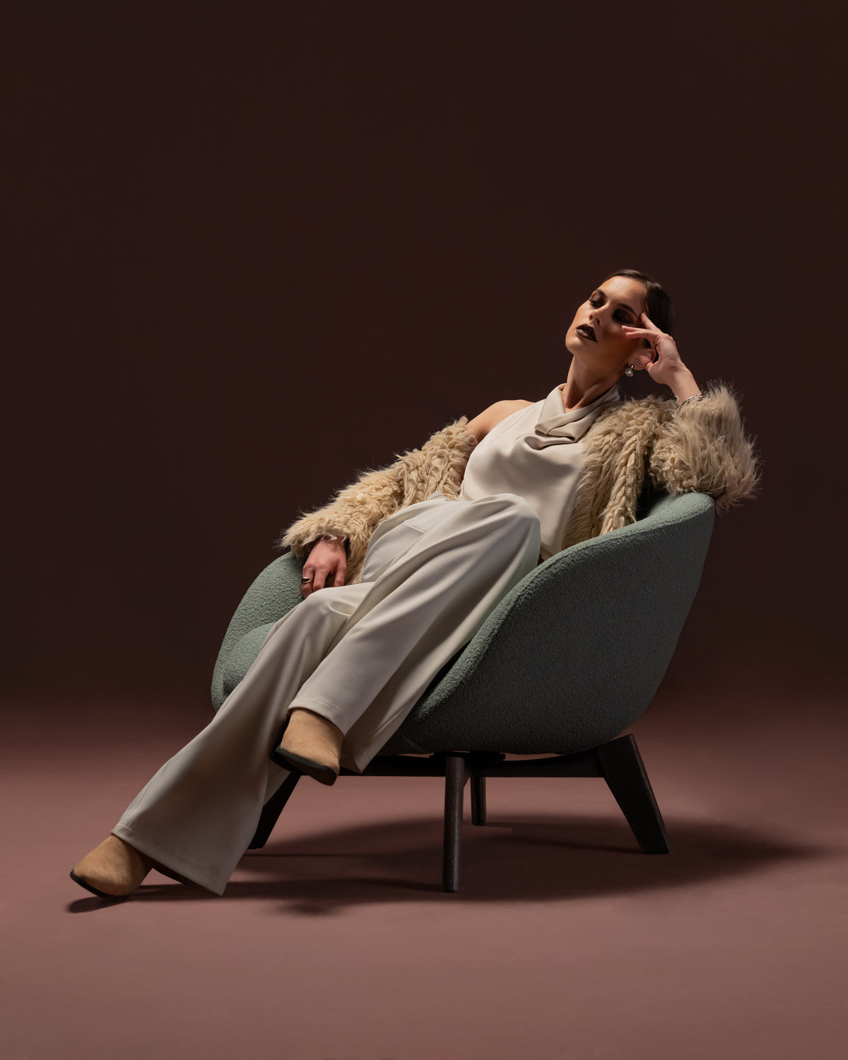 Model reclining in the Darby armchair upholstered in textured green fabric with rounded form and solid oak leg base.