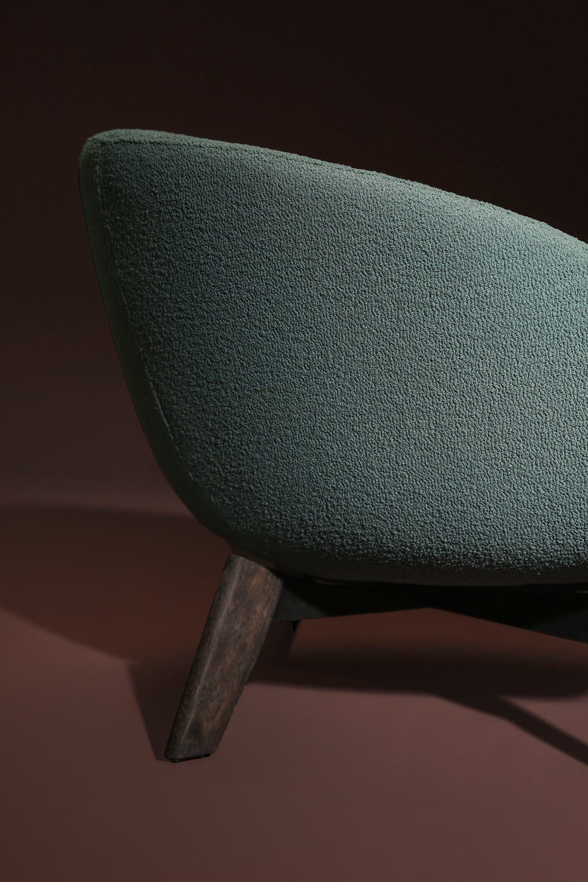 Close-up of the Darby armchair showing its curved teal upholstered back and angled solid wood leg.