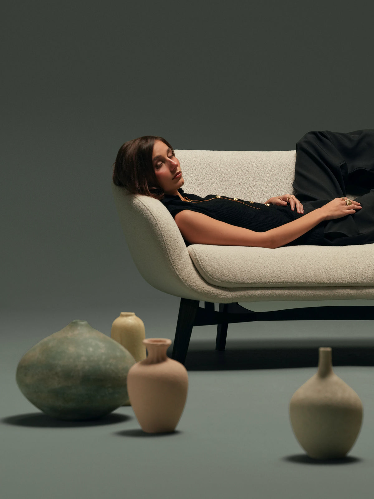 Woman reclining on the beige Darby sofa, showing its supportive seat cushion, curved backrest, and compact proportions.