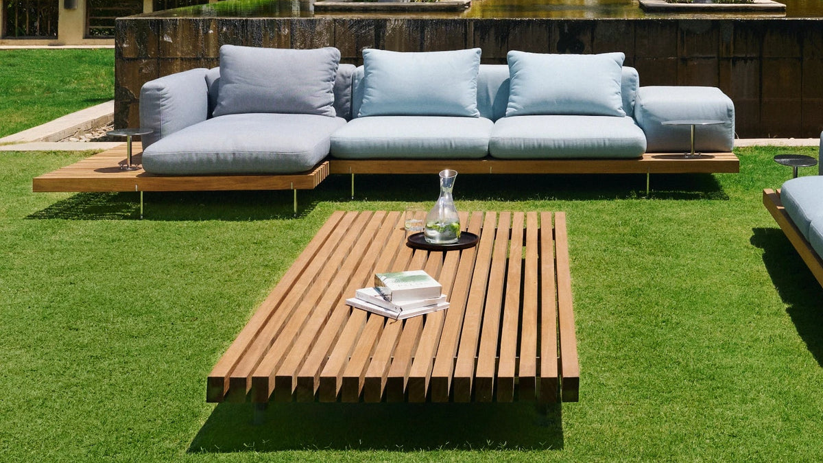 Blue Dock outdoor sofas arranged around a slatted solid teak Dock table on a garden lawn.