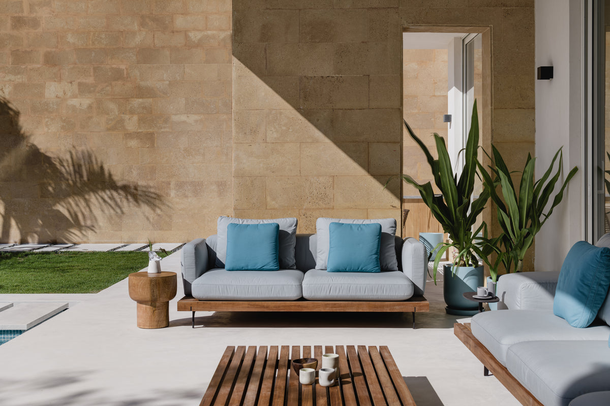 Grey Dock outdoor sofa with blue cushions paired with a slatted teak Dock table on a modern patio.