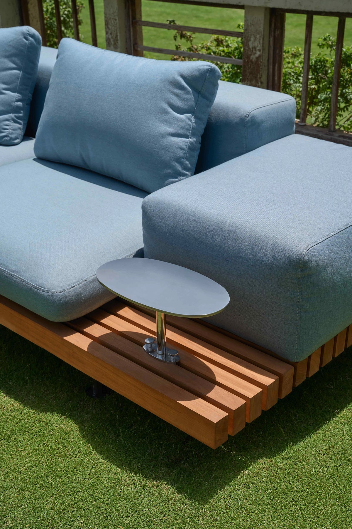 Close-up of the blue Dock outdoor sofa with a slatted teak platform and integrated round stainless steel accent table.