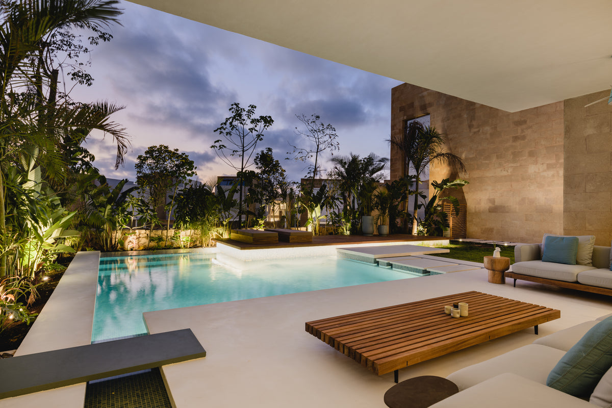 Slatted solid teak Dock table paired with coordinating outdoor seating beside a swimming pool at dusk.