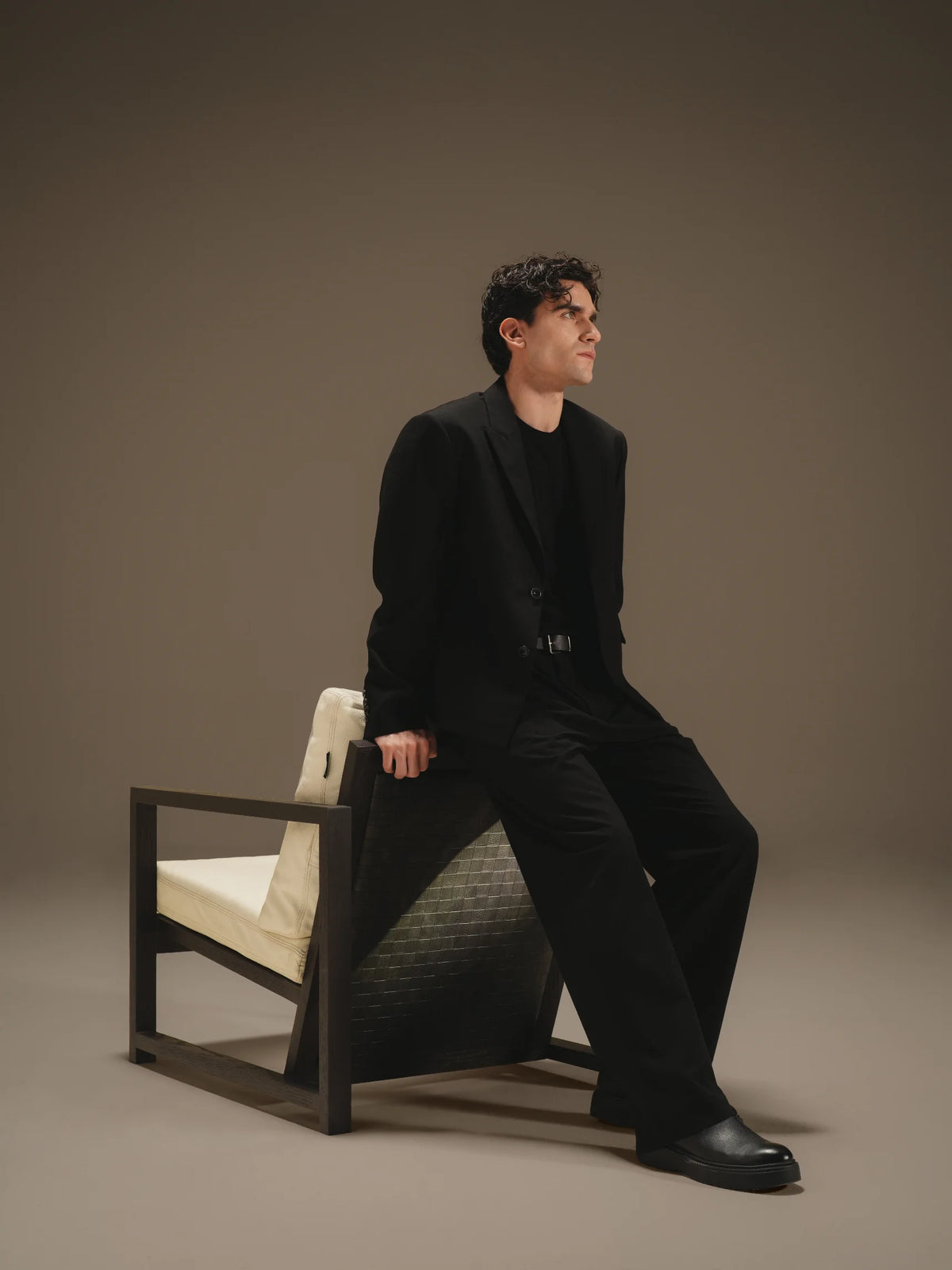 Man seated on the Easy Slanted chair, shown from behind with its angled frame and contrasting woven leather back panel.