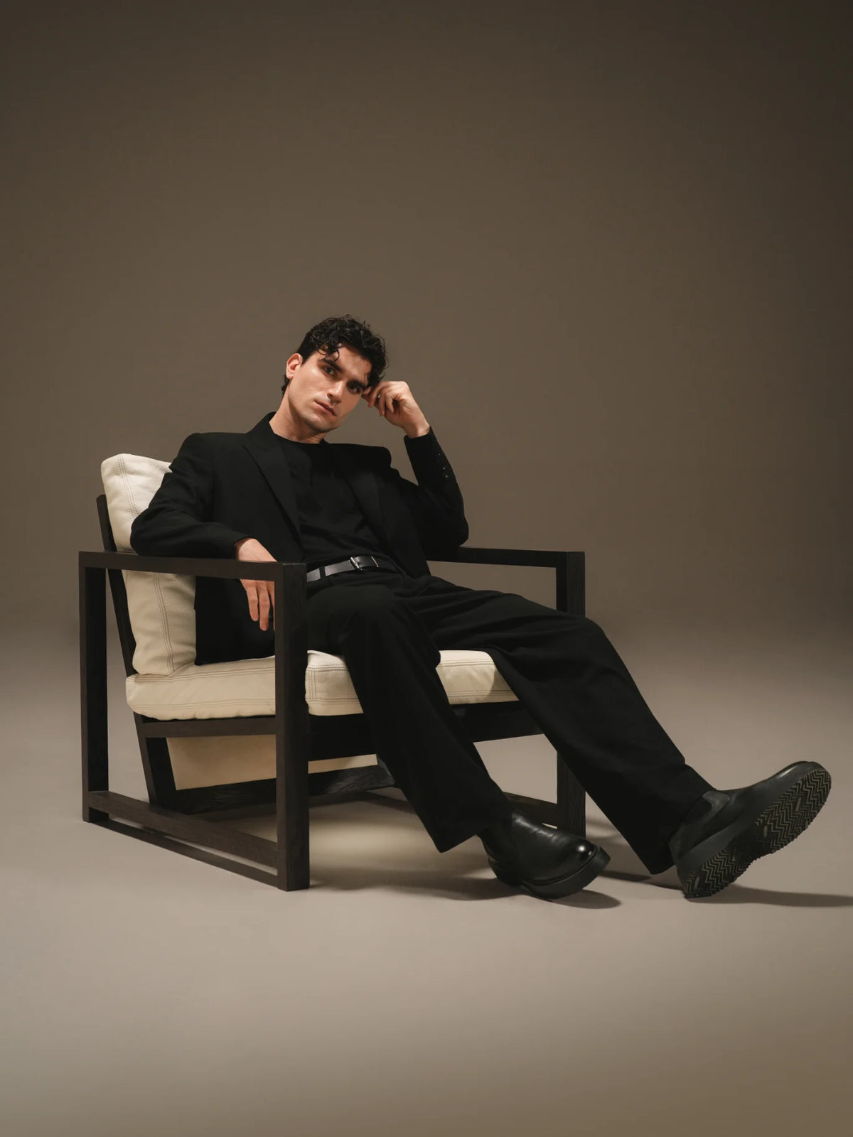 Man seated in the beige Easy Slanted lounge chair, featuring a reclined backrest and dark solid wood frame.