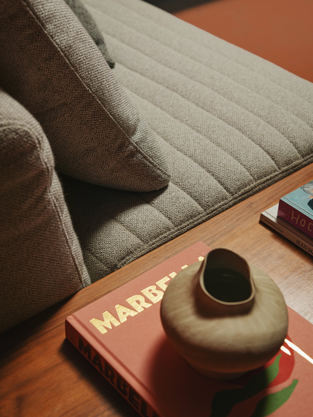 Close-up of the beige Edge sofa showing its textured upholstery, inverted seam stitching, back cushions, and integrated wooden table.
