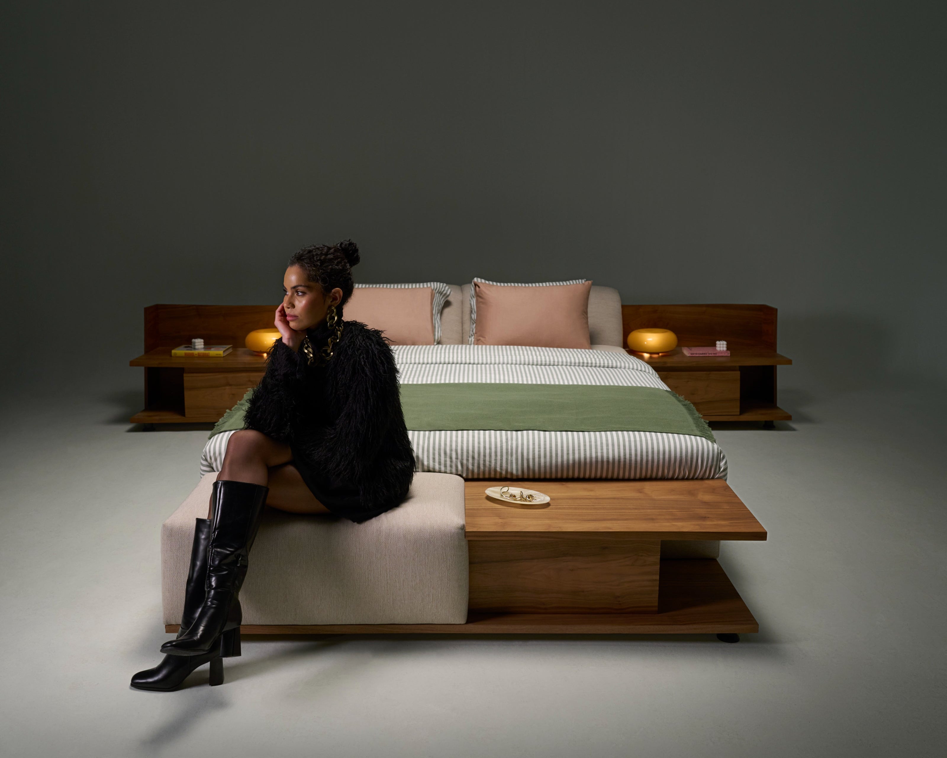 Model seated on Estrella Bed featuring slim adjustable headrest, platform mattress base, and wooden banquette with padded seat.
