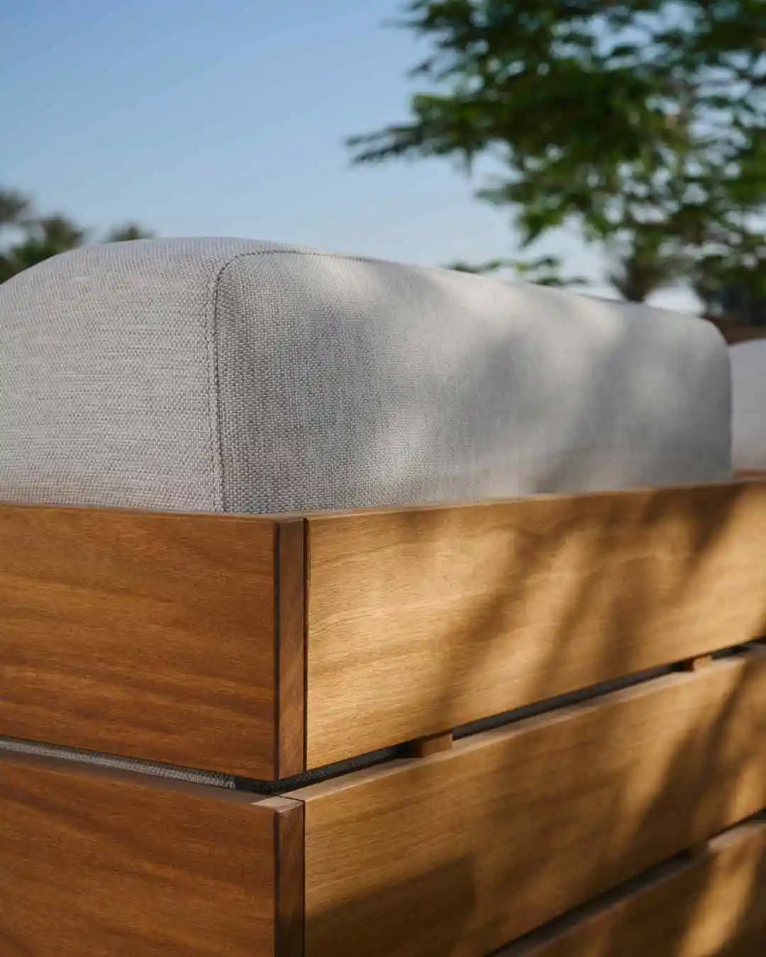 Close-up of the Fatty outdoor sofa’s contoured upholstered backrest enclosed by its solid teak slab frame.