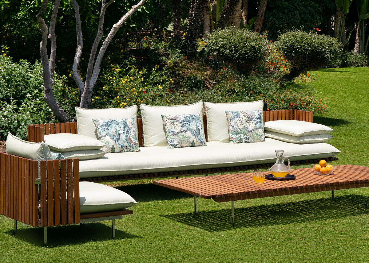 Fence outdoor sofa and armchair with vertical teak slat frames and cream cushions, paired with a matching slatted teak coffee table in a garden.