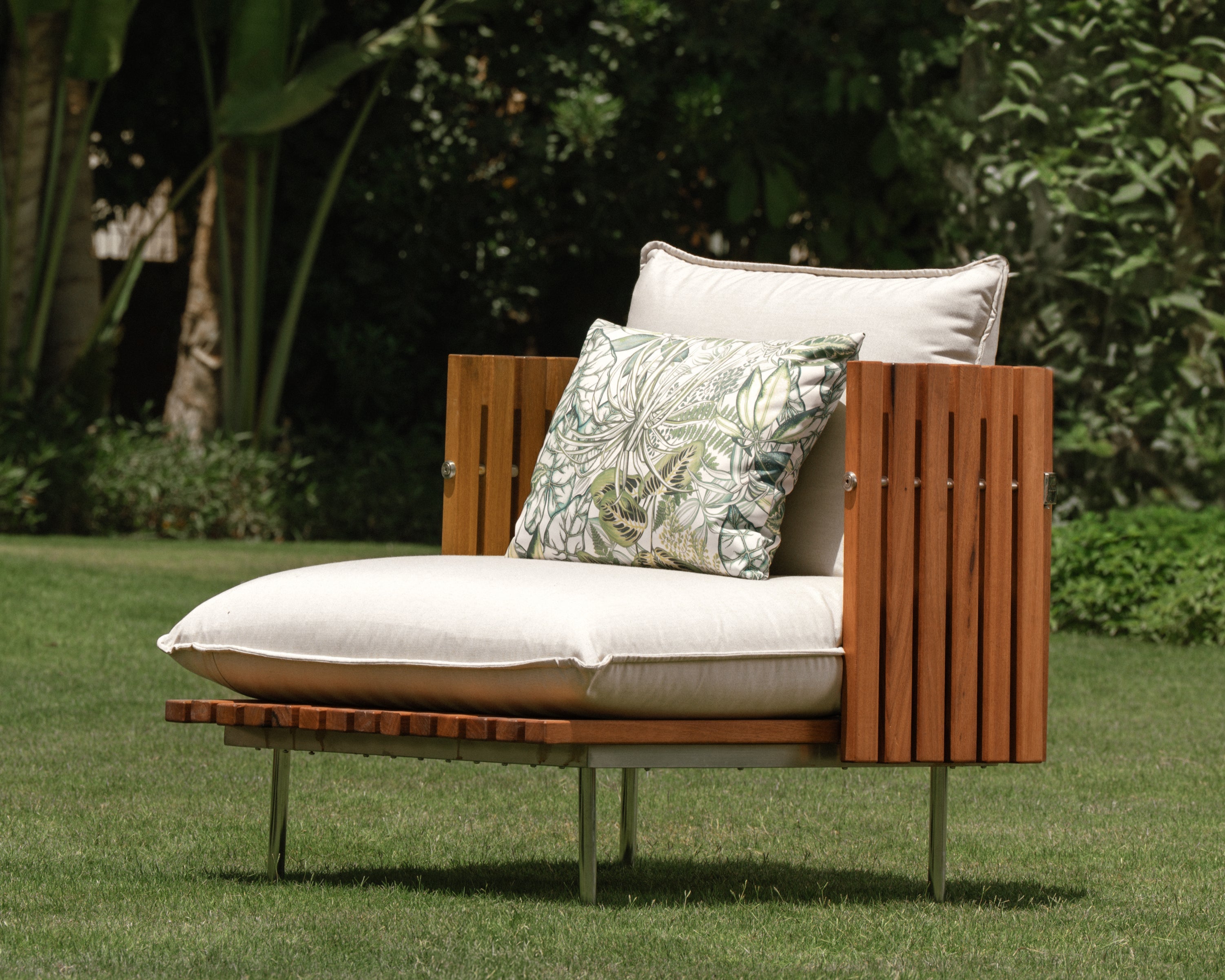 Fence armchair with teak wood slatted sides, cream upholstered cushions, and stainless steel legs, styled outdoors on a garden lawn.