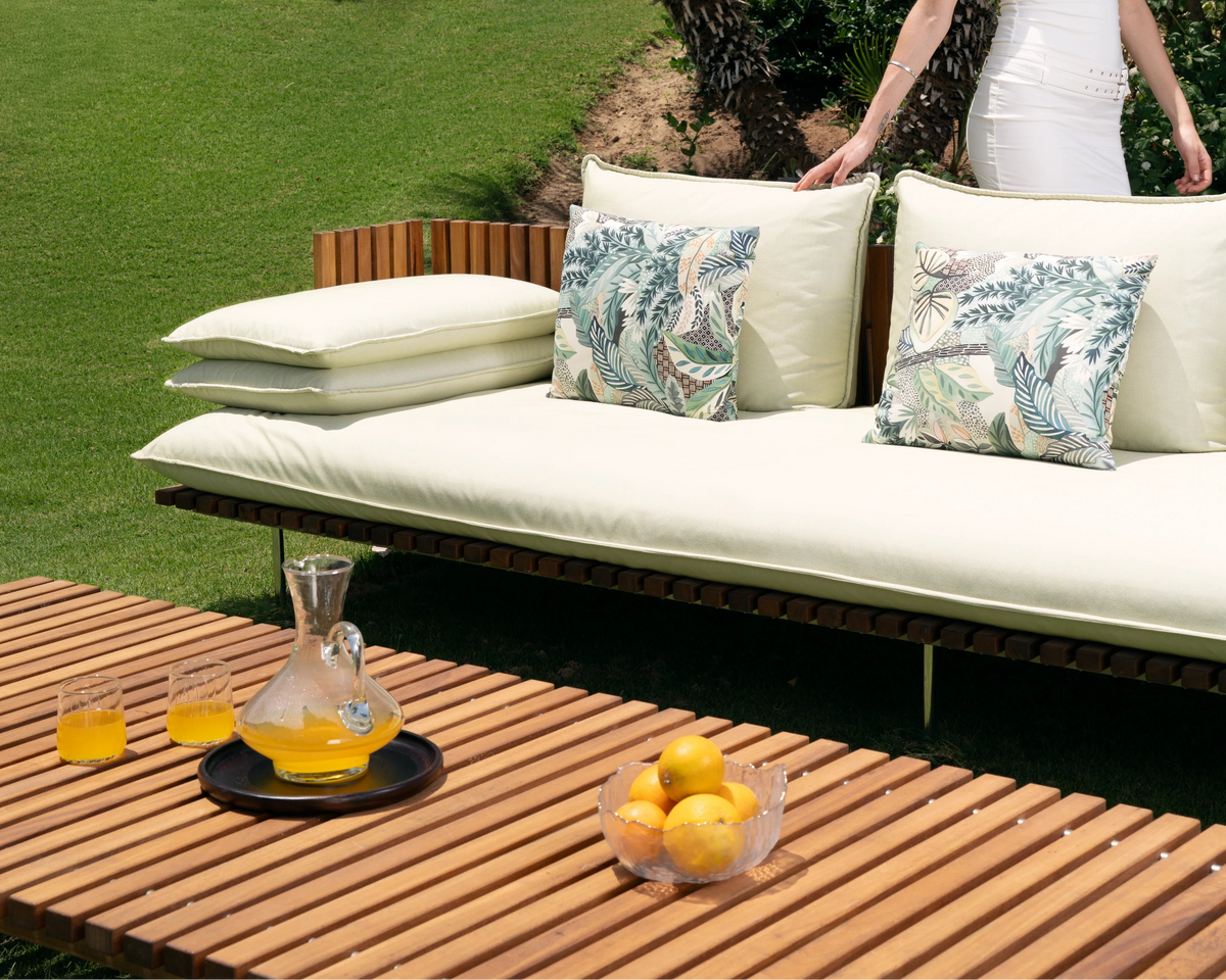 Front view of Fence sofa in cream upholstery with teak slatted side panels and stainless steel legs, styled outdoors on a garden lawn.