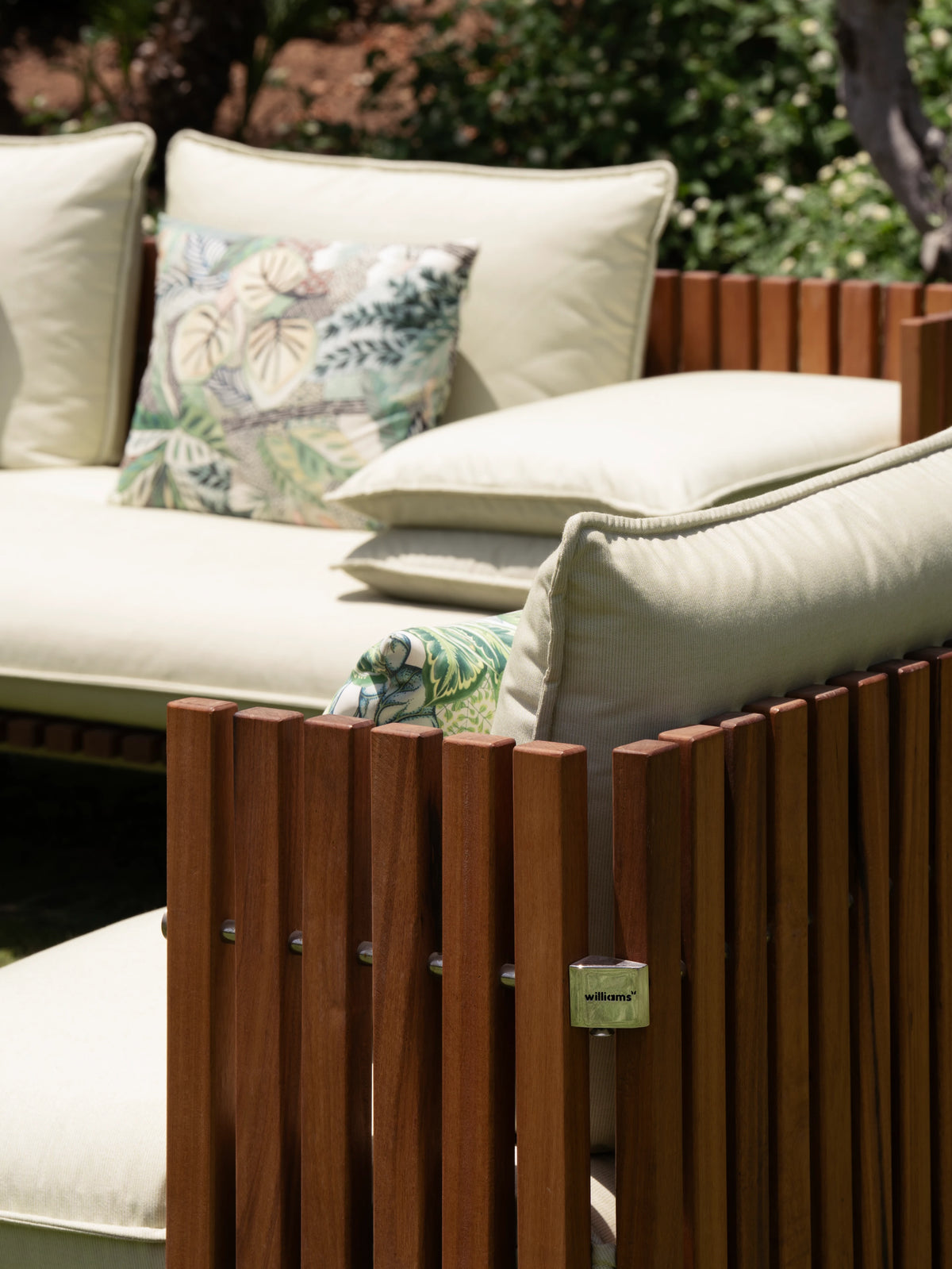 Close view of the Fence outdoor sofa showing its cream cushions, French seams, vertical teak slats and stainless steel connectors.
