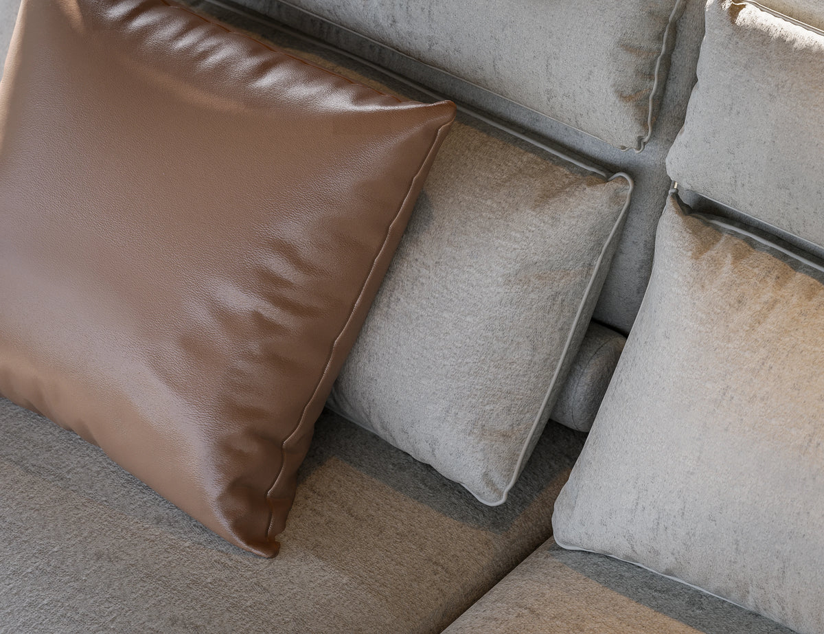 Close-up of a beige Flexor Sofa with piped cushions, a lumbar bolster, and a contrasting brown accent cushion.