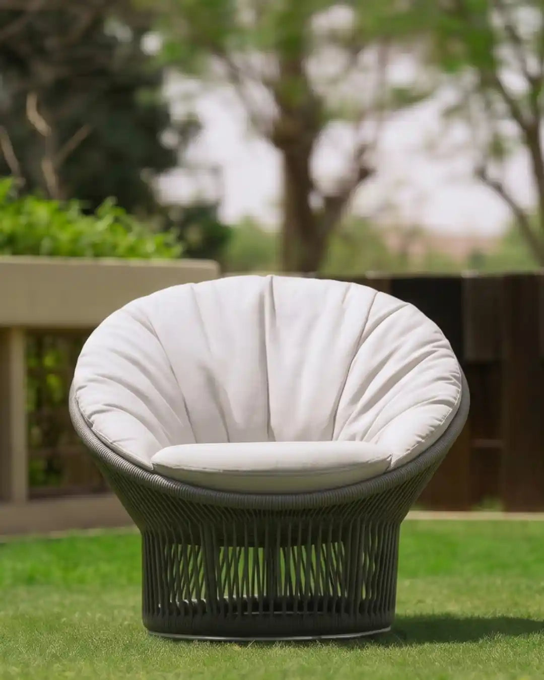 Front view of the Sun outdoor armchair with a circular dark grey rope frame and generously padded light cushion on a green lawn.