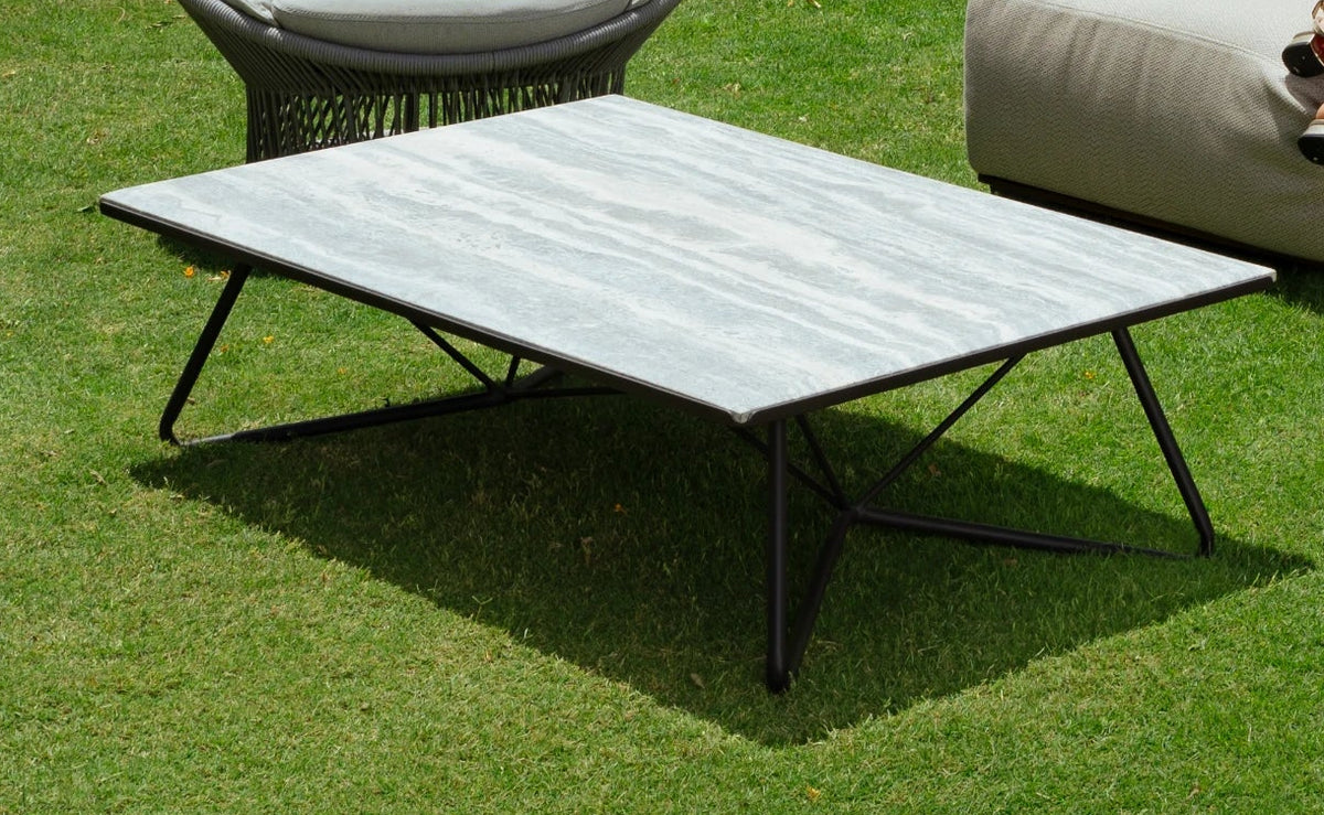 Close view of the Geo outdoor coffee table featuring a rectangular light stone top and an open black crisscross metal base on a garden lawn.