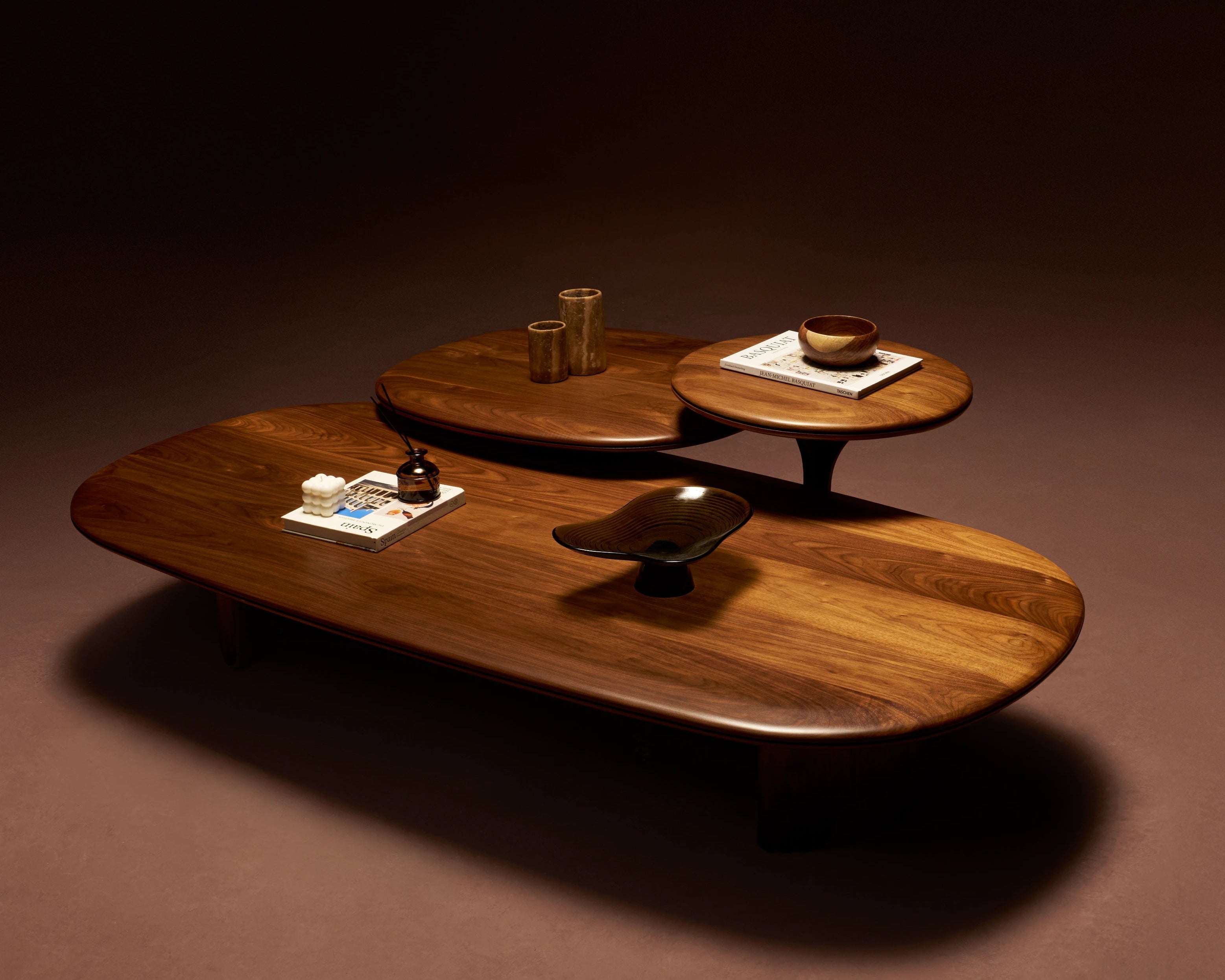 Set of three Glide solid walnut coffee tables in different sizes, featuring rounded tops with a central-split carved detail and tapered edges.