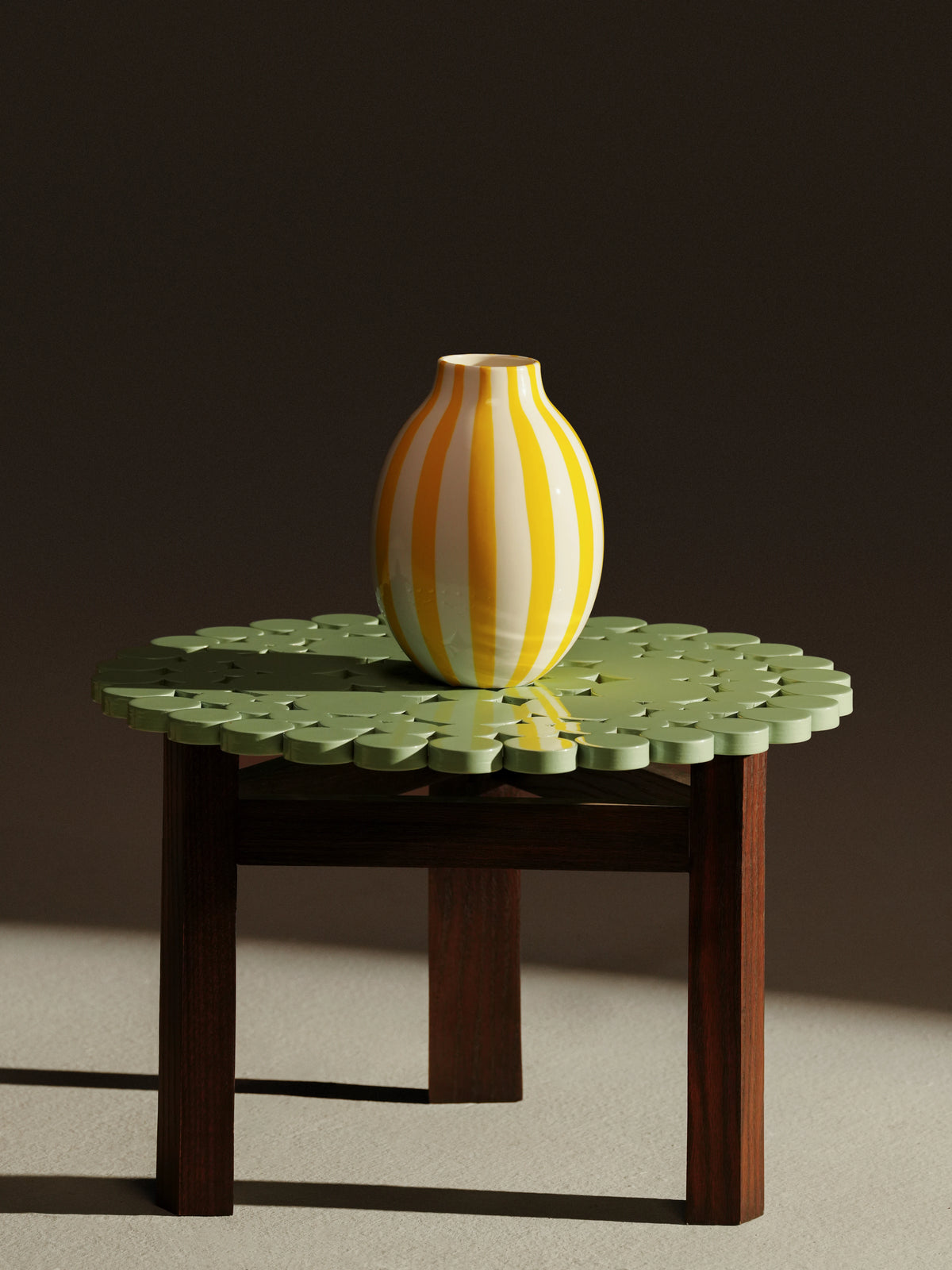 Green Blossom accent table with a decorative cutout top, three solid wood legs, and a striped ceramic vase.