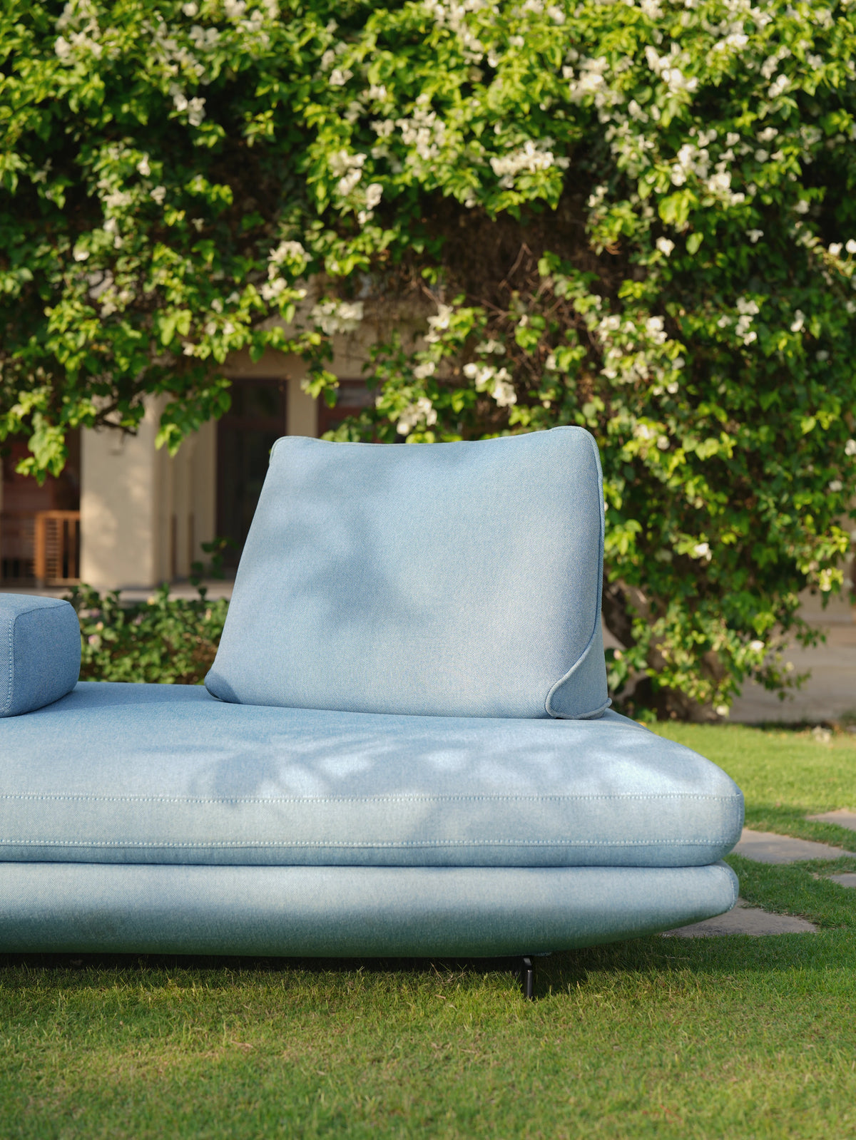 Close view of the light blue Island outdoor sofa showing its piped seat and repositionable back cushion on a garden lawn.