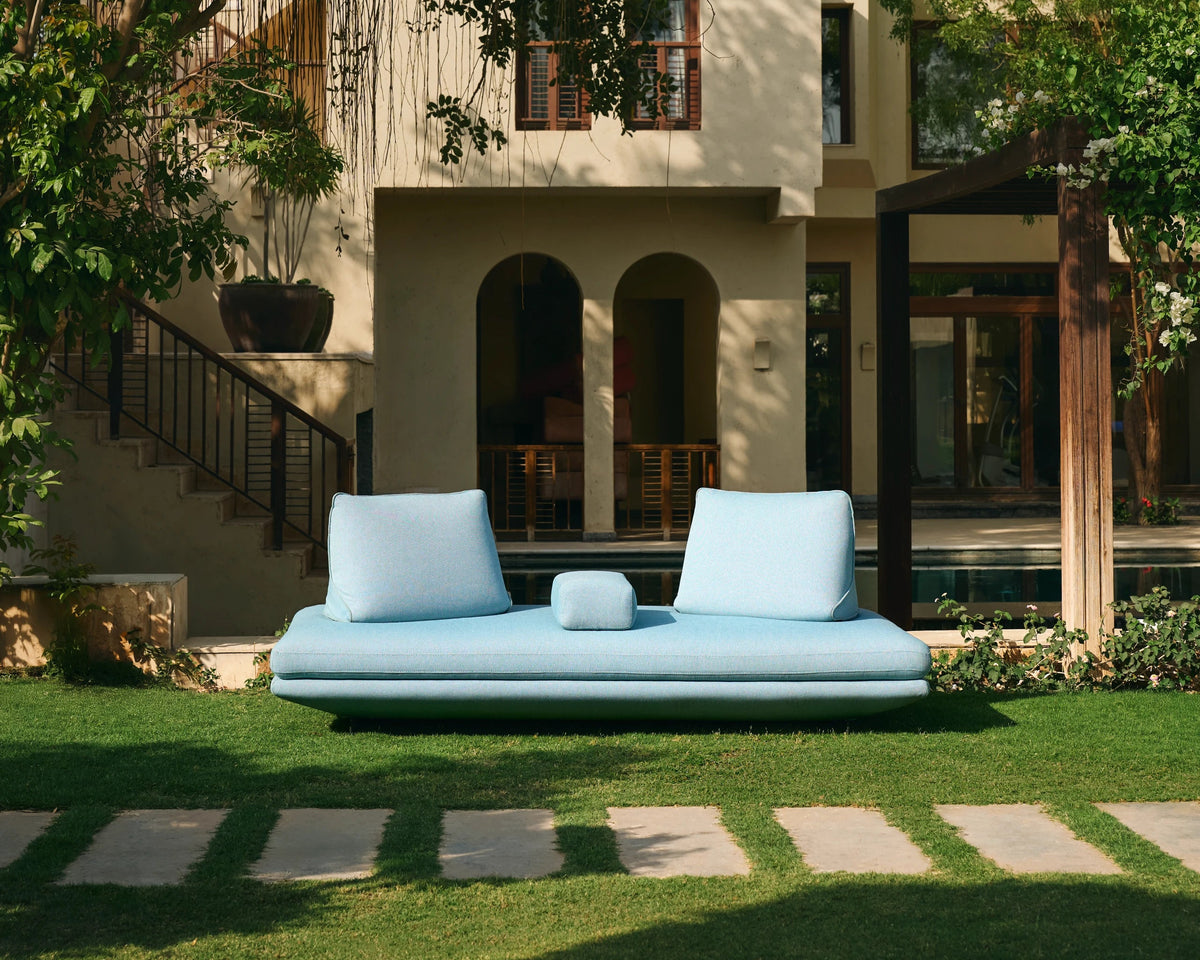 Light blue Island outdoor sofa with two repositionable back cushions, set on a garden lawn beside a swimming pool.