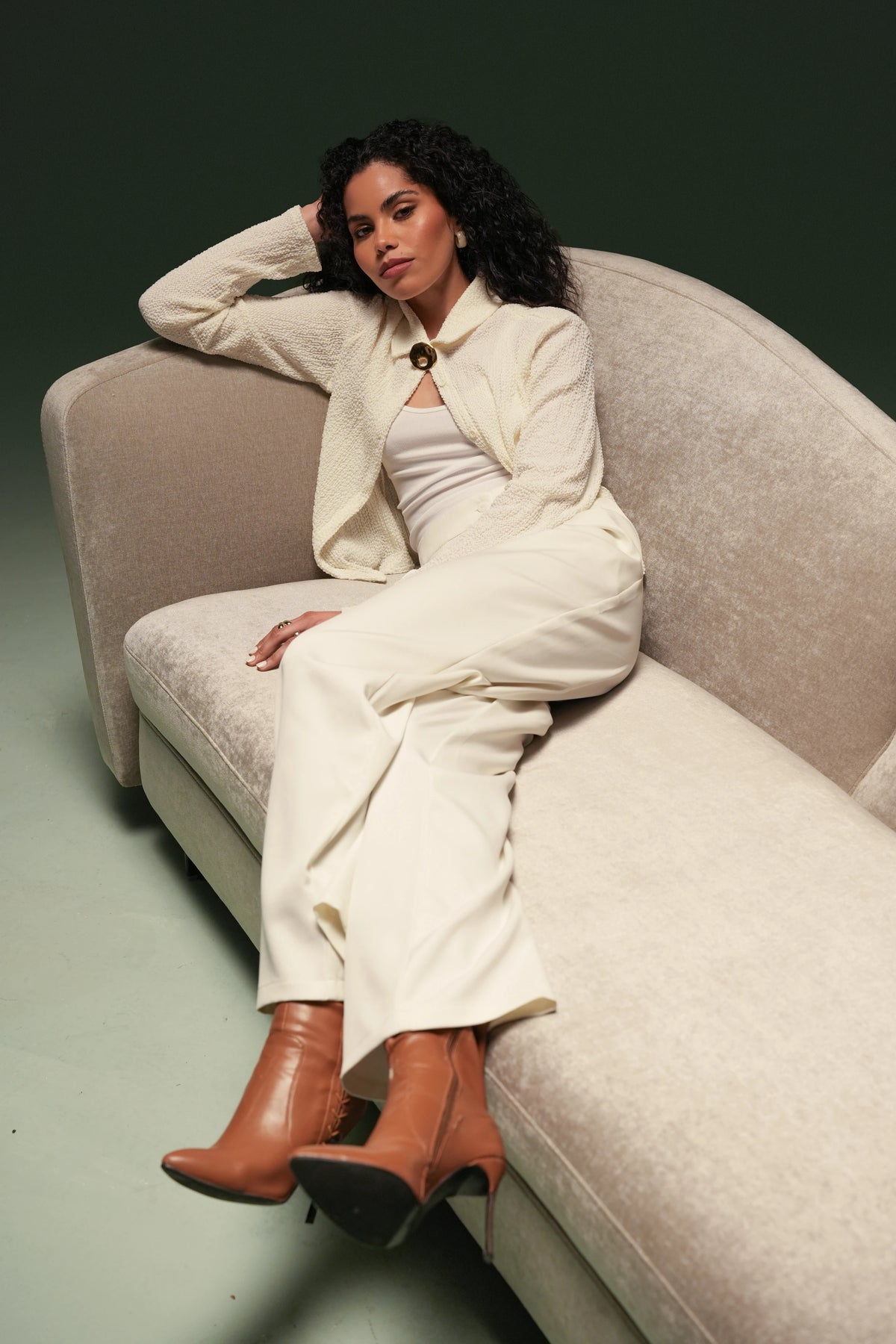 Woman seated on the beige Kirby sofa, framed by its asymmetrical backrest that curves from high to low.
