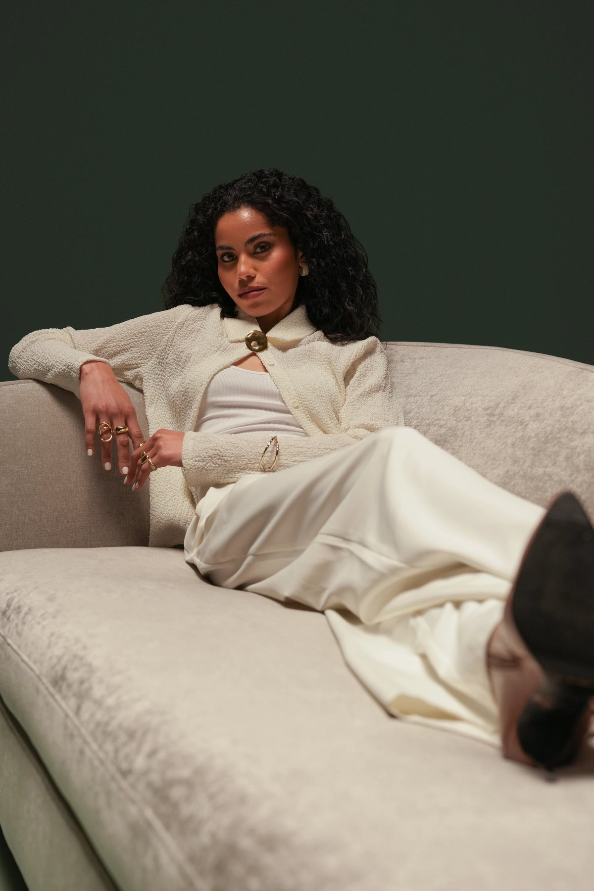 Woman reclining on the cream Kirby sofa with a deep seat and asymmetrical curved backrest against a dark green background.