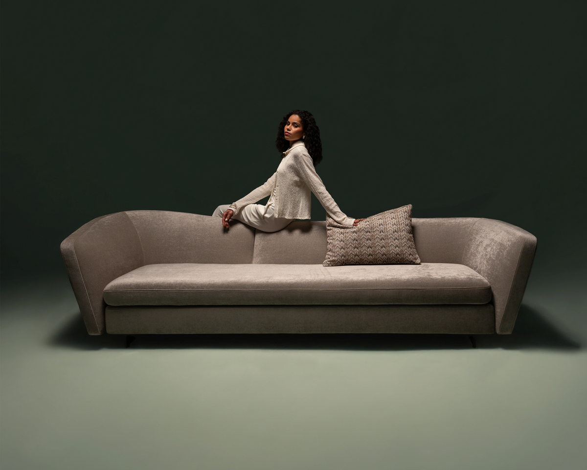 Kirby sofa with curved frame and dual-high back in beige upholstery, styled against a dark backdrop in a modern lifestyle setting.