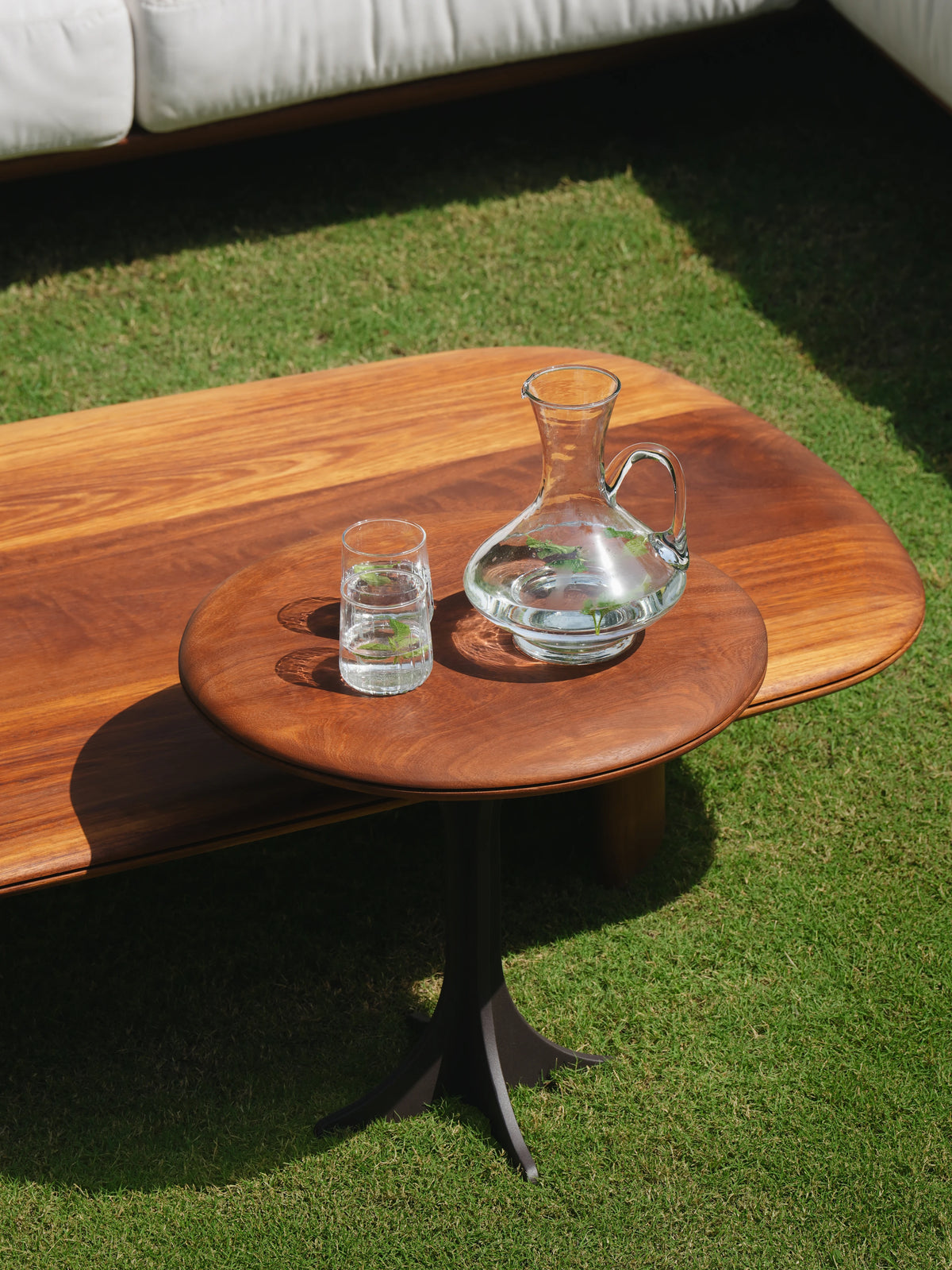 Large solid teak Glide coffee table paired with a small round Glide accent table featuring a teak top and dark metal base.