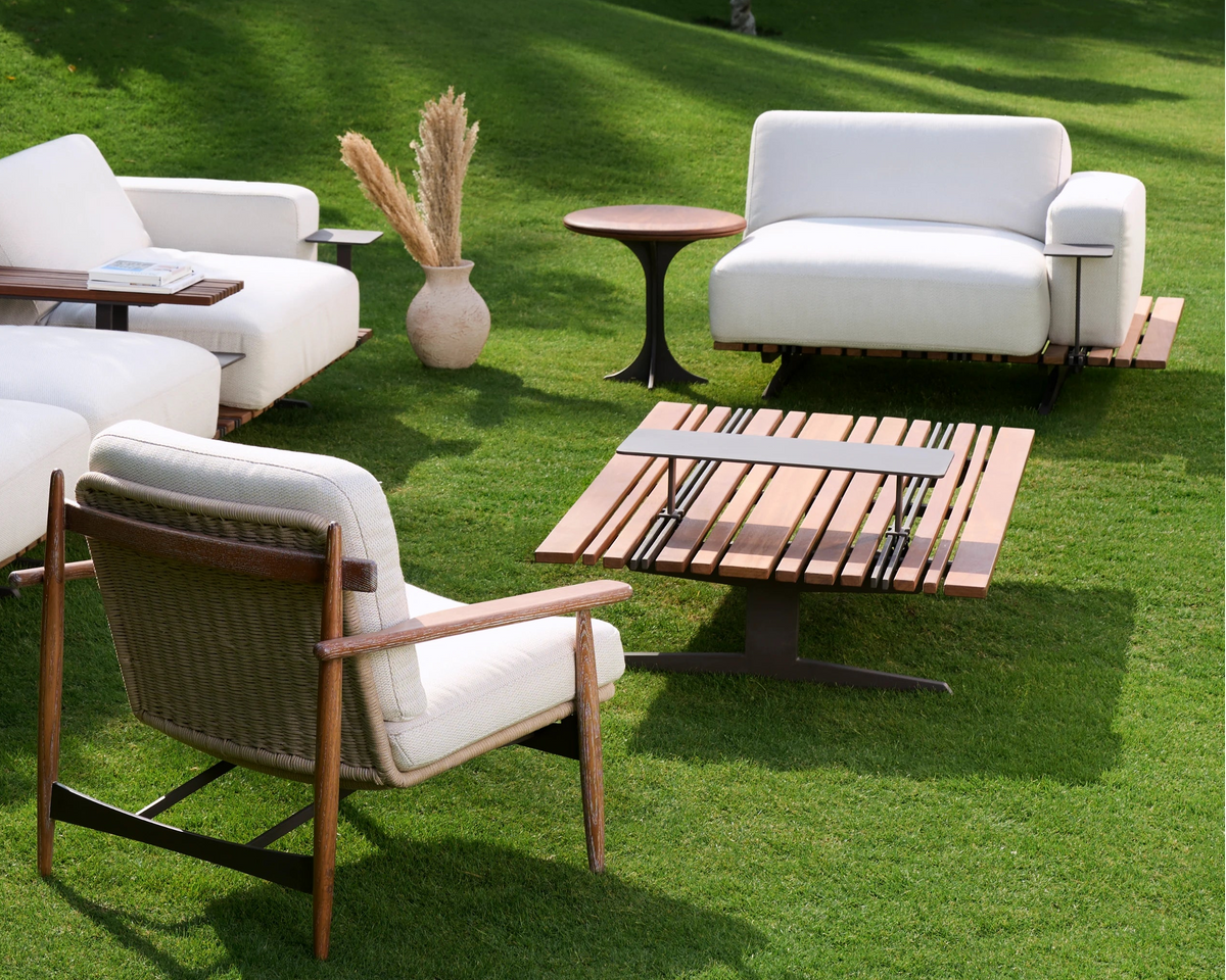 Lodge outdoor table with a teak slatted top and stainless steel details, arranged with white Lodge seating and a Retro armchair on a garden lawn.
