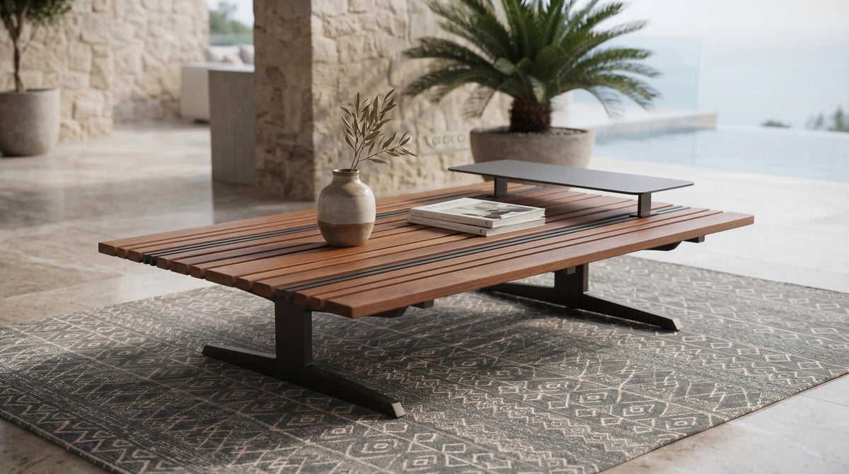 Lodge outdoor coffee table featuring mixed-width teak slats, stainless steel inlays, and a raised accent table on a covered stone patio.